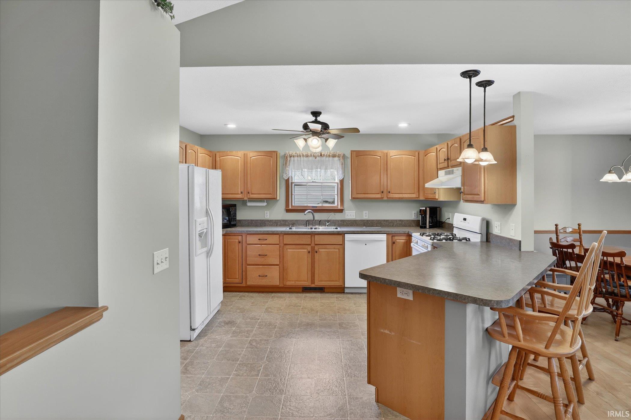 Kitchen featuring light wood cabinetry, stone-finish countertops, tile flooring, and a breakfast bar with pendant lighting