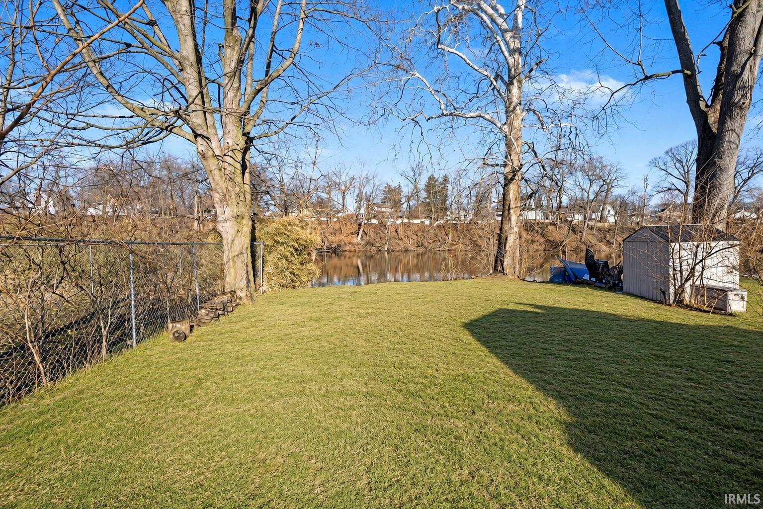 Expansive green lawn with mature trees and a chain-link fence