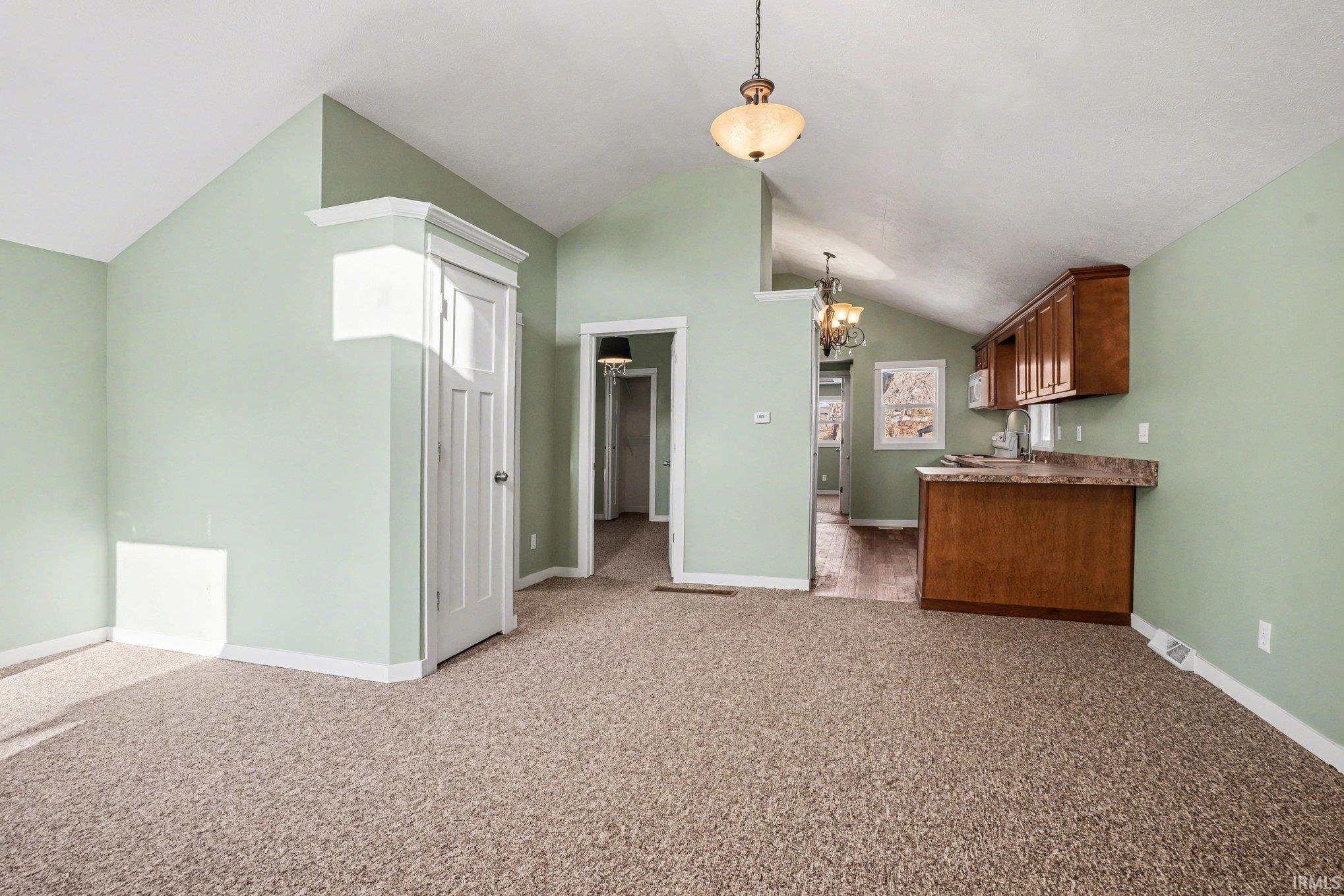 Kitchen with hanging lights, lofted ceiling, dark colored carpet, and wood finish cabinets