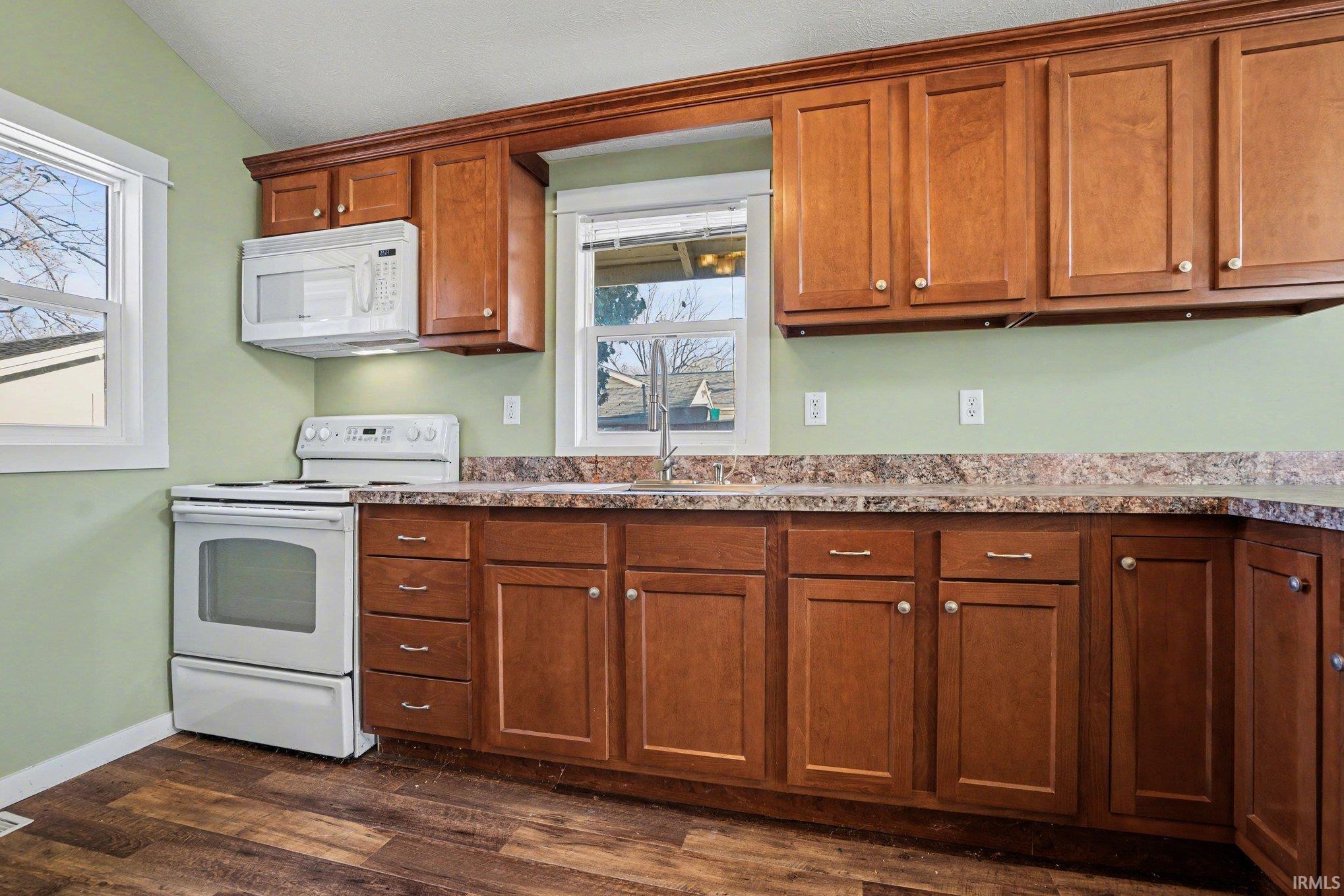 Kitchen featuring white appliances, wood finish cabinets, dark wood-type flooring, light countertops, and lofted ceiling
