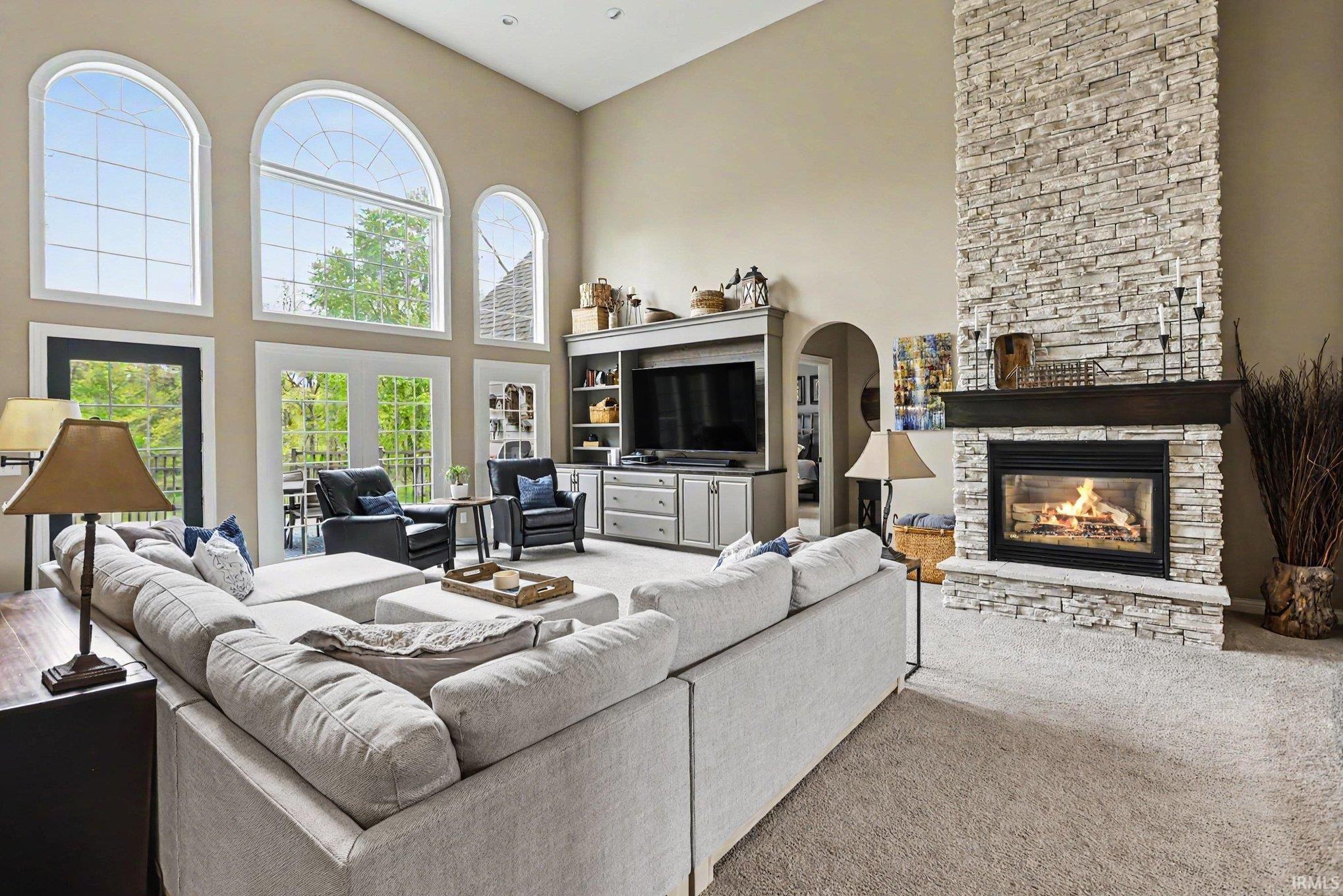 Living area featuring a floor-to-ceiling stone fireplace, high ceilings, a wall of arched and rectangular windows, a built-in media center, and light-colored carpeting