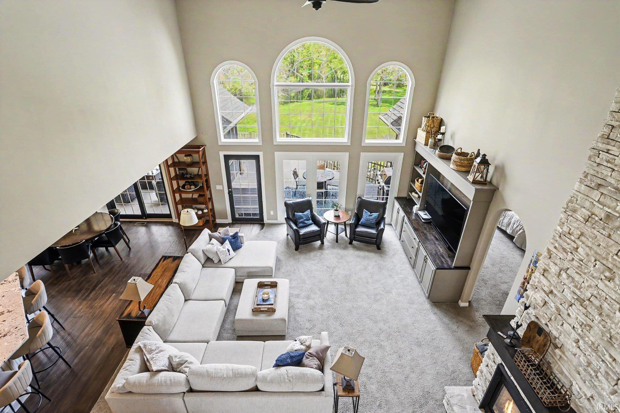 Spacious living area featuring a two-story ceiling, arched windows, built-in entertainment cabinetry, a stacked stone fireplace, and wood-finish flooring in the adjacent dining area