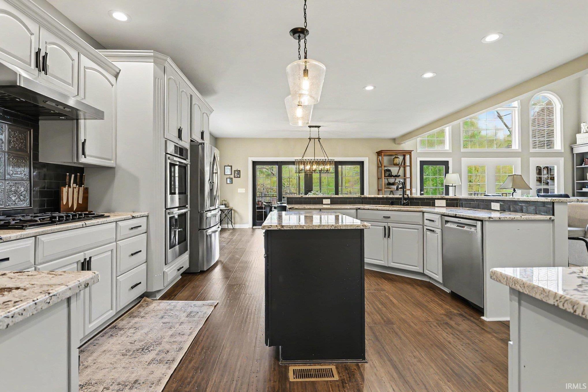 Open-concept kitchen featuring light-colored cabinetry with dark hardware, stainless steel appliances, and wood-finish flooring
