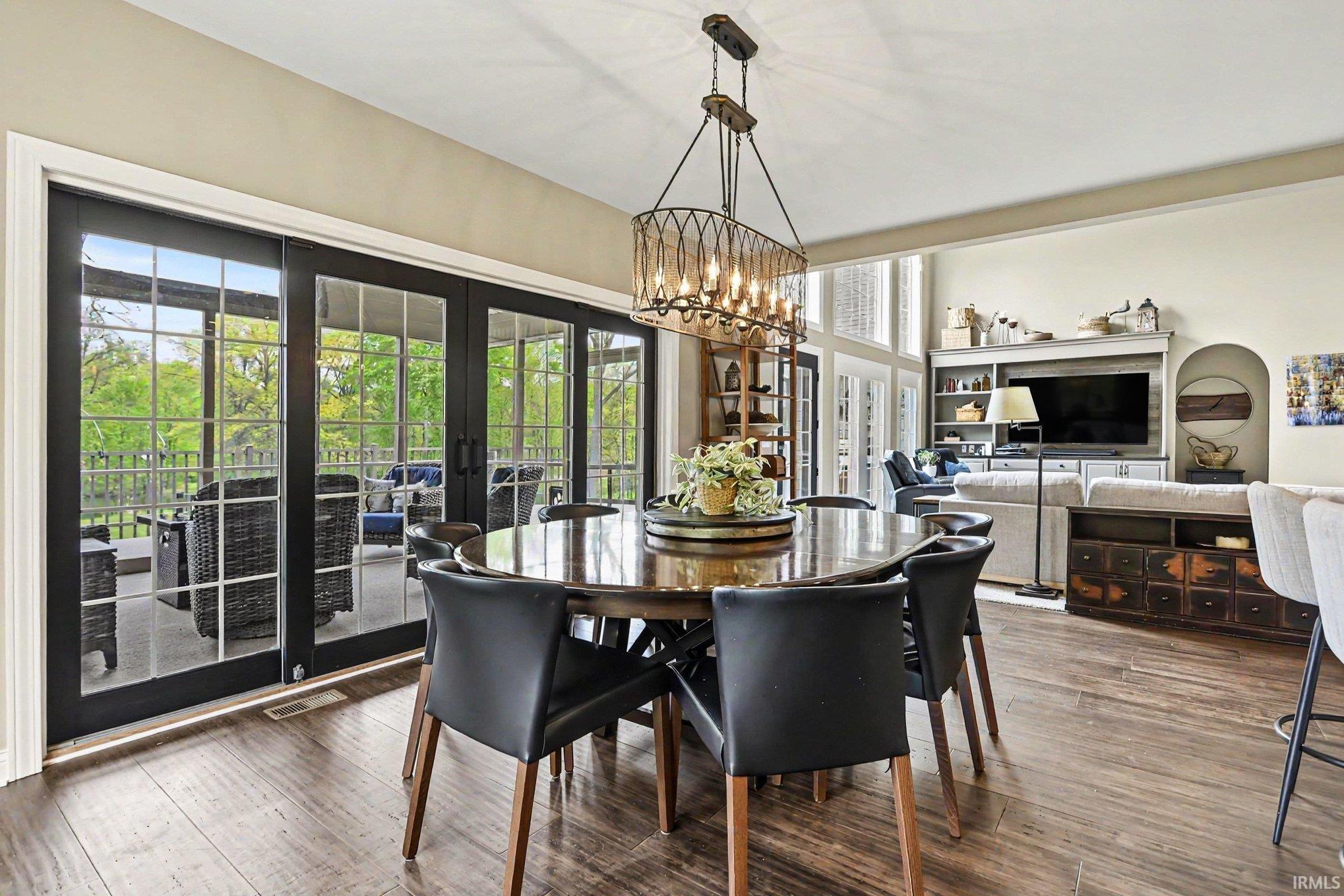 Dining area with a sophisticated chandelier, dark wood-finish flooring, and multiple glass-paneled doors leading to an outdoor patio