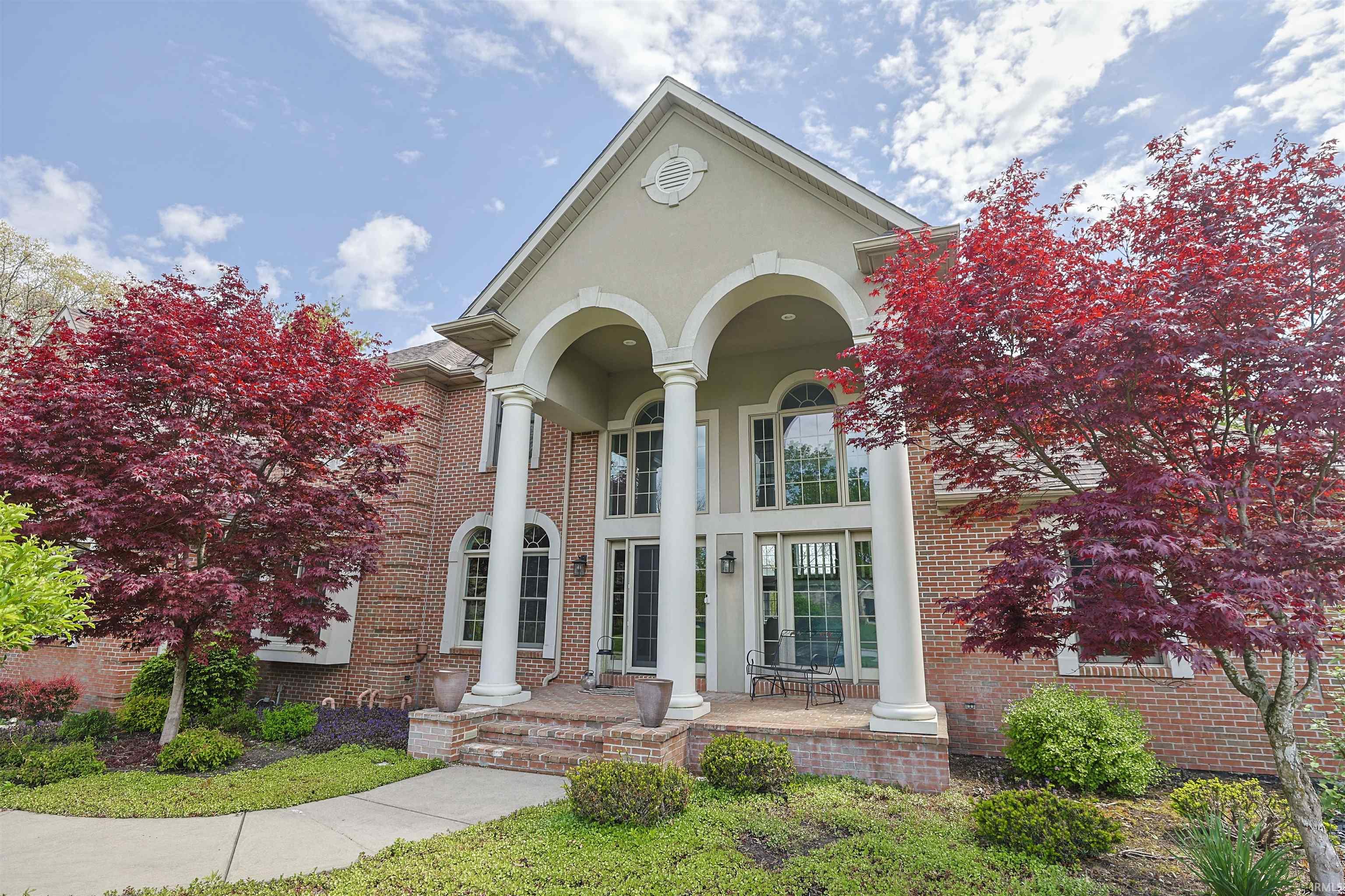 Brick facade residence featuring a grand arched portico with classical columns, a multi-pane glass entry door, arched windows, and extensive landscaping