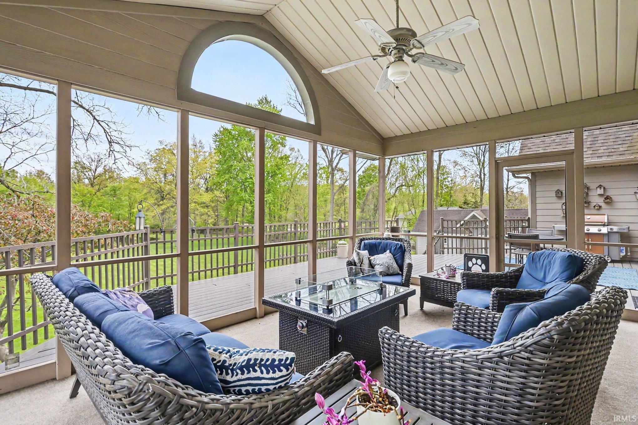 Screened-in porch featuring a vaulted ceiling with a fan light fixture, an arched transom window, and a wood-finish deck