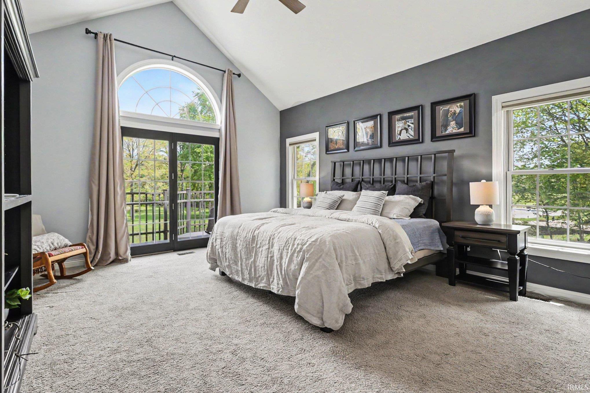 Vaulted ceiling bedroom featuring a dark accent wall, light-toned carpeting, and a ceiling fan