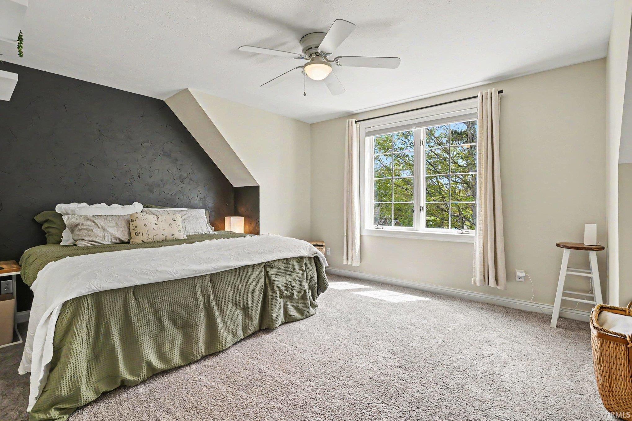 Spacious room featuring textured accent wall, light-toned carpeting, window with grid panes, recessed ceiling, and a ceiling fan with integrated lighting