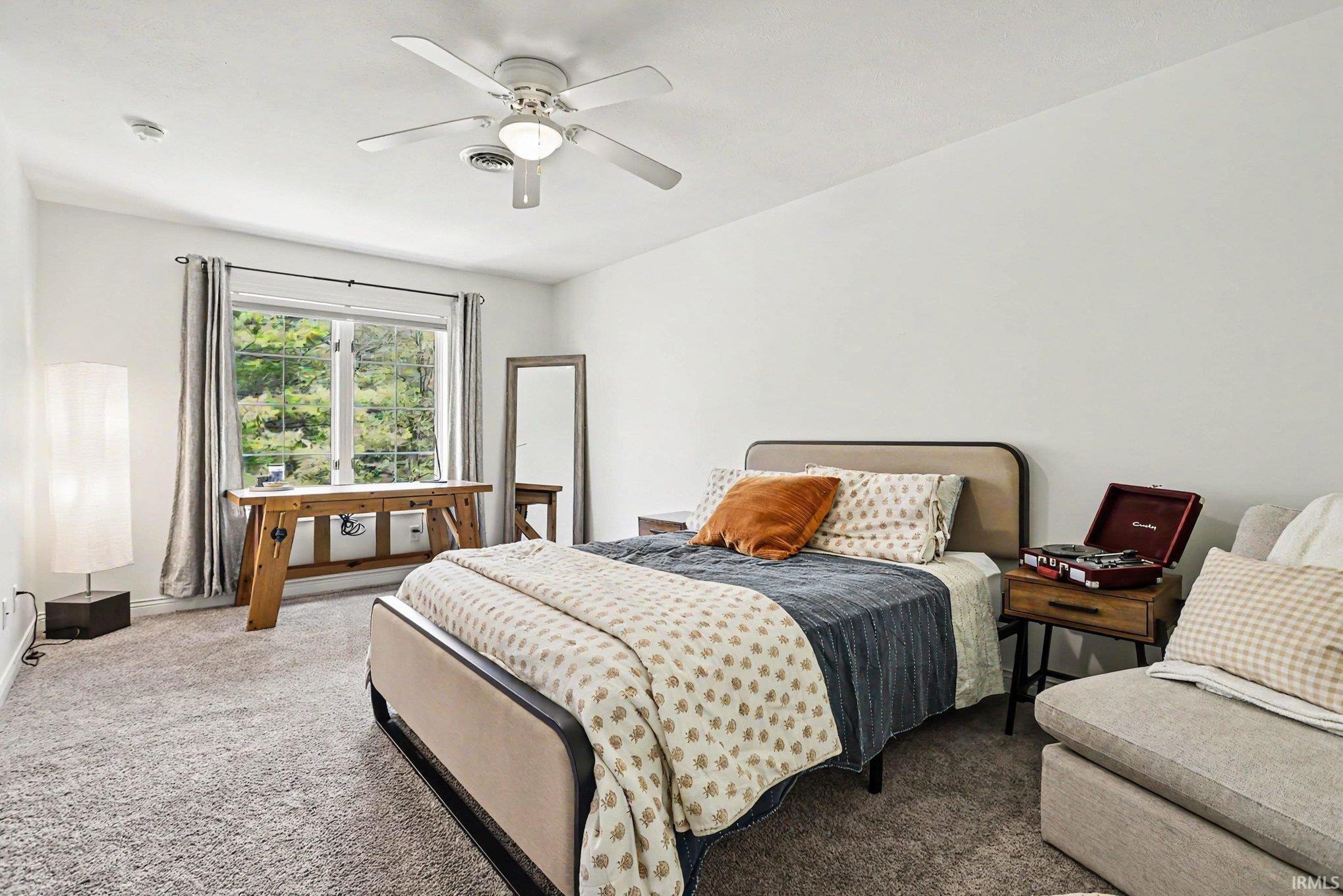 Carpeted room featuring a double window with a wooded backdrop, a ceiling fan with integrated lighting, and a built-in smoke detector