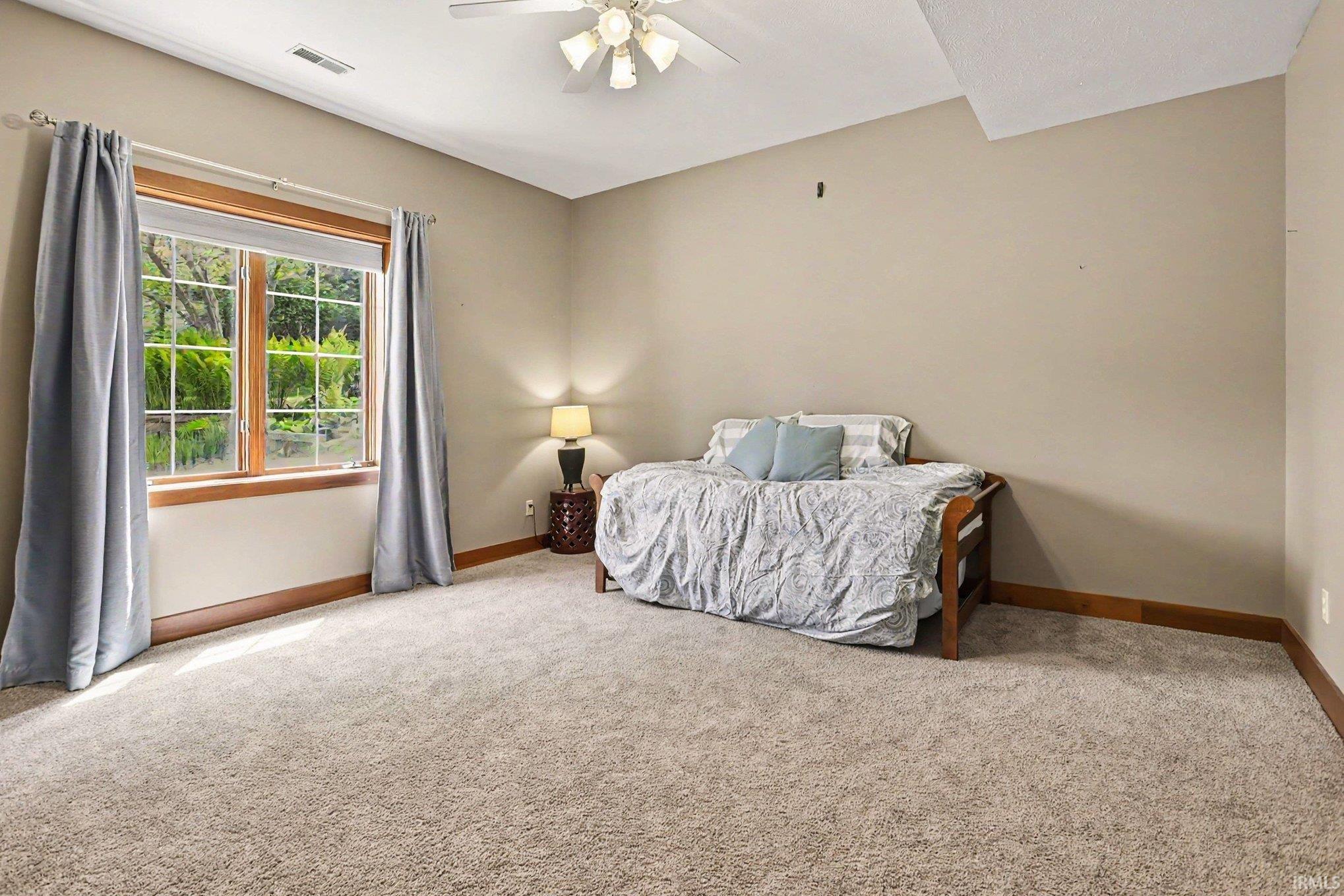 Carpeted room featuring a large window with natural wood trim, a ceiling fan, and painted walls