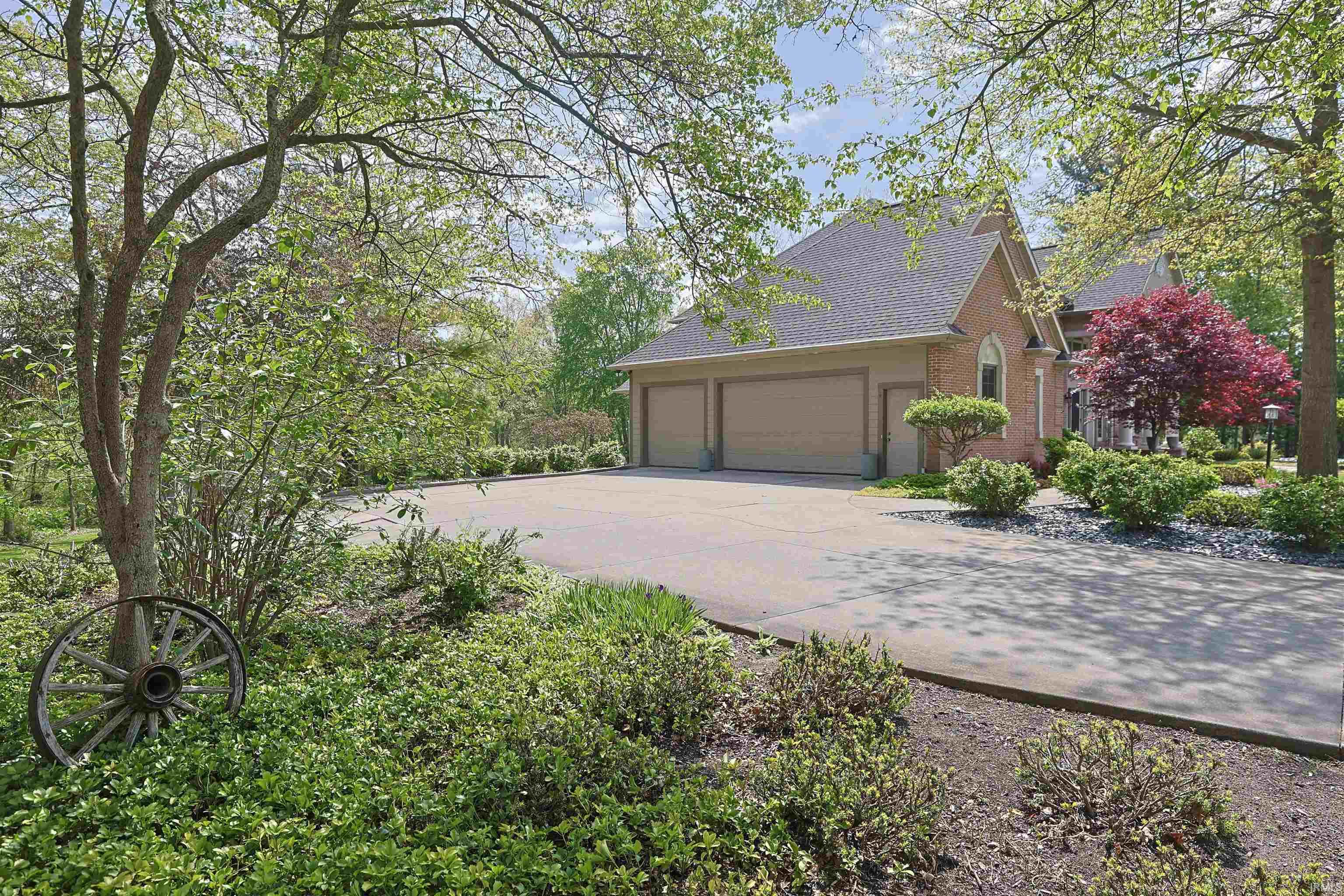 Brick exterior with a three-car garage, expansive paved driveway, and mature trees