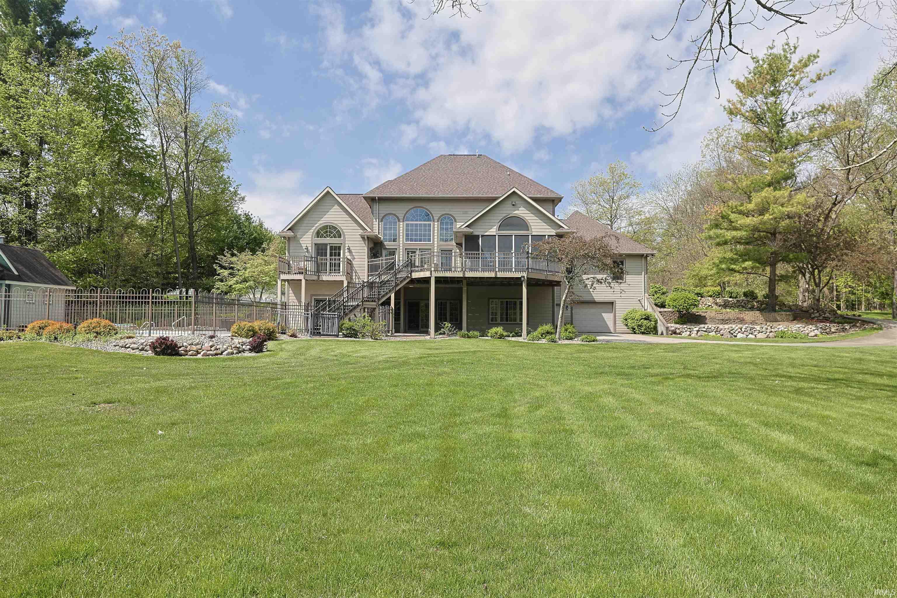 Spacious rear exterior featuring an expansive lawn, multi-level decks, a screened-in porch, and an in-ground pool with surrounding fencing