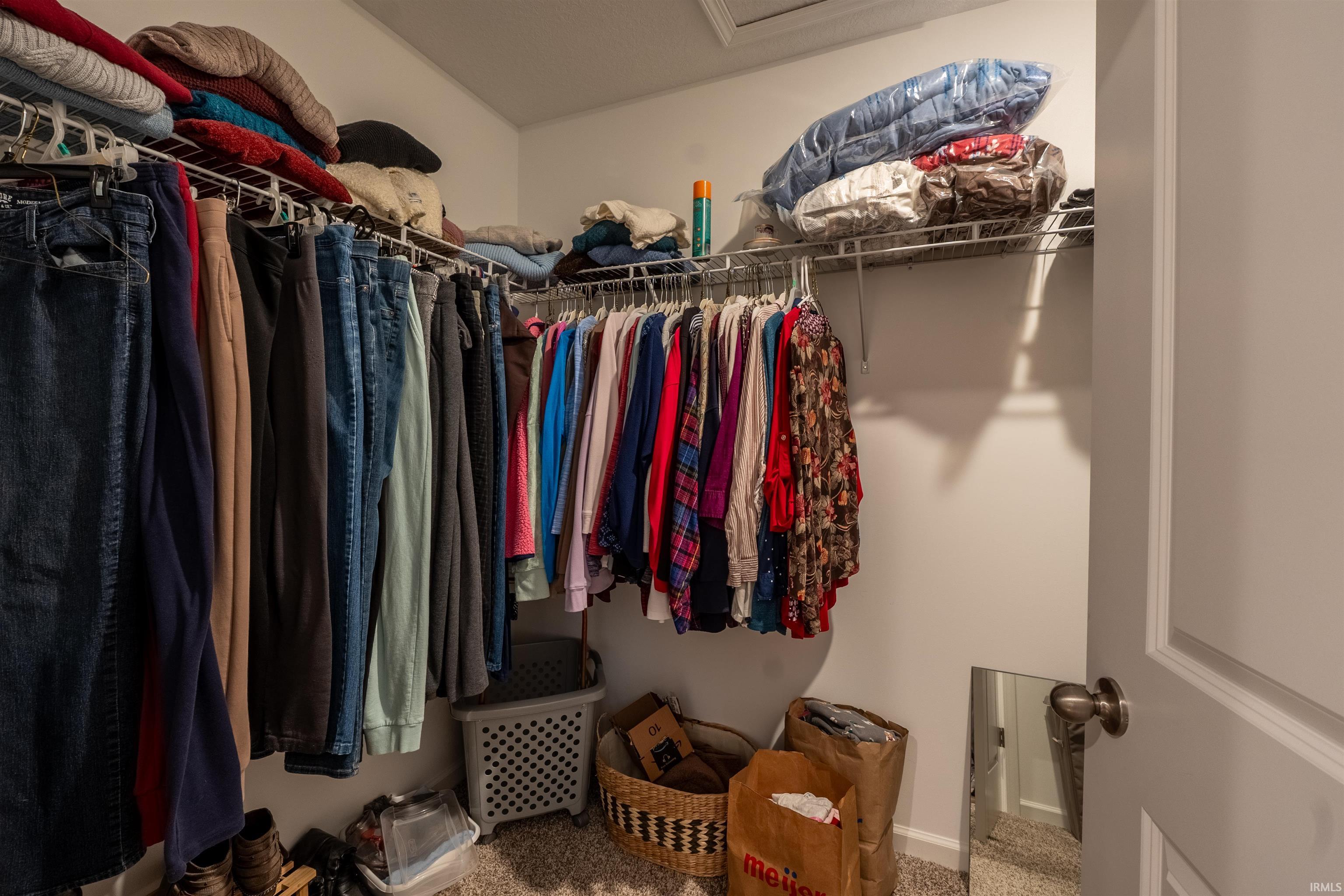 Walk-in closet featuring wire shelving, multiple hanging rods, wall-to-wall carpeting, and a white paneled door with a brushed nickel knob