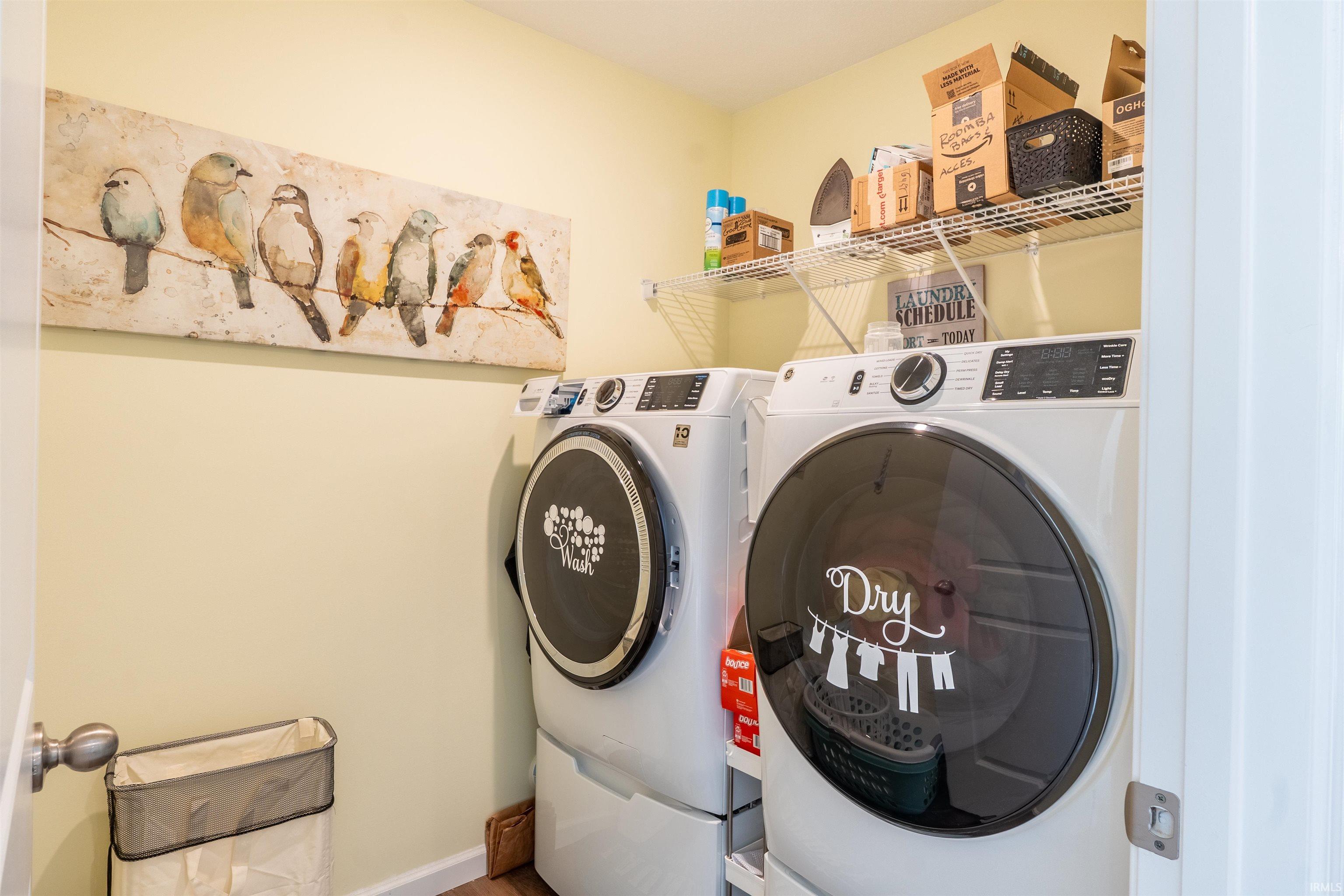 Dedicated laundry area featuring a white front-load washer and dryer set, integrated storage shelving, and light-toned wall paint