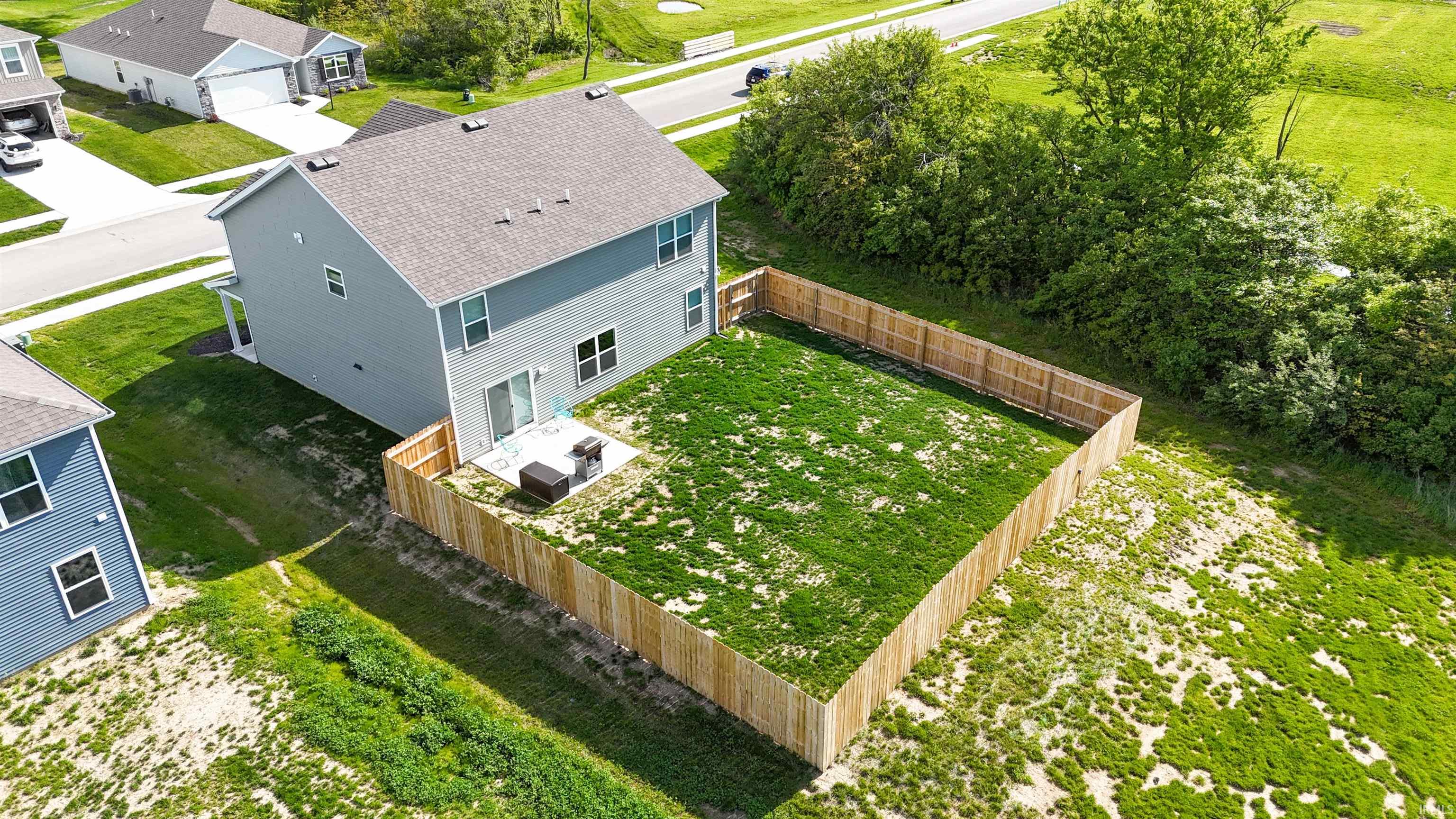 Expansive fenced backyard with a patio, featuring a light gray two-story exterior and sliding glass doors