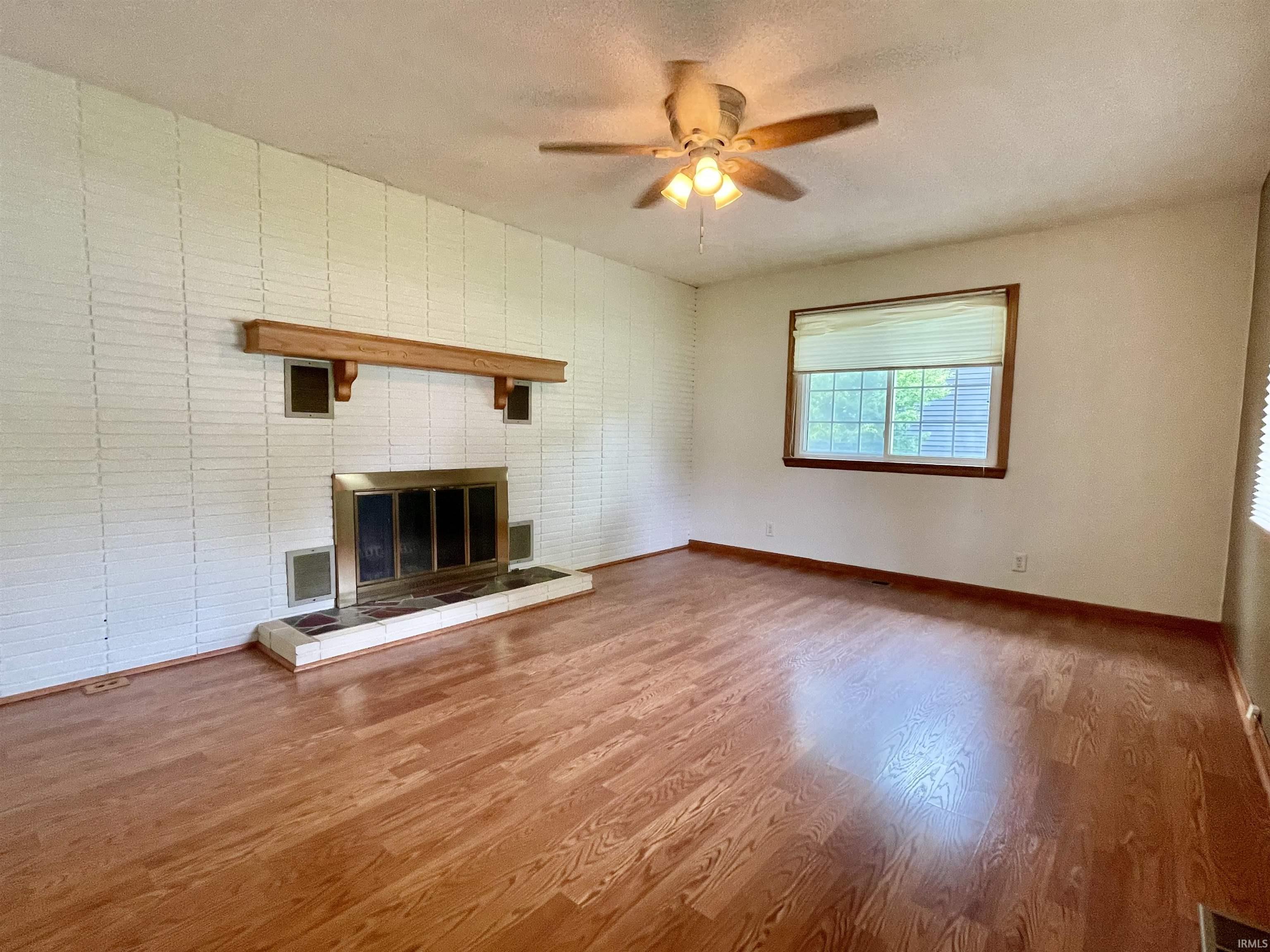 Spacious room featuring wood-finish flooring and a white painted brick fireplace with a wood mantel