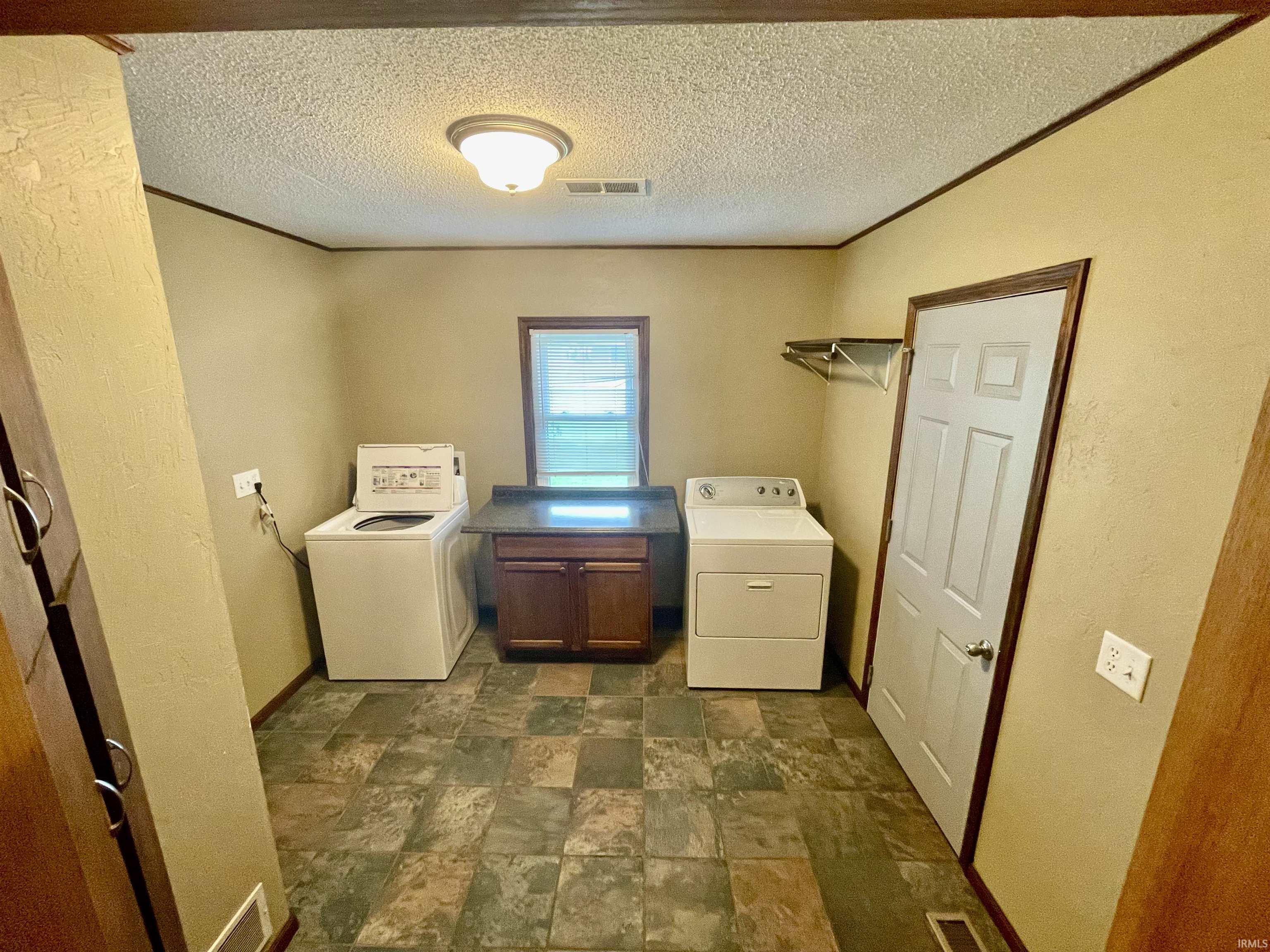 Laundry room featuring patterned tile flooring, wood-finish trim, a built-in wood-finish cabinet with a dark countertop, and a window providing natural light