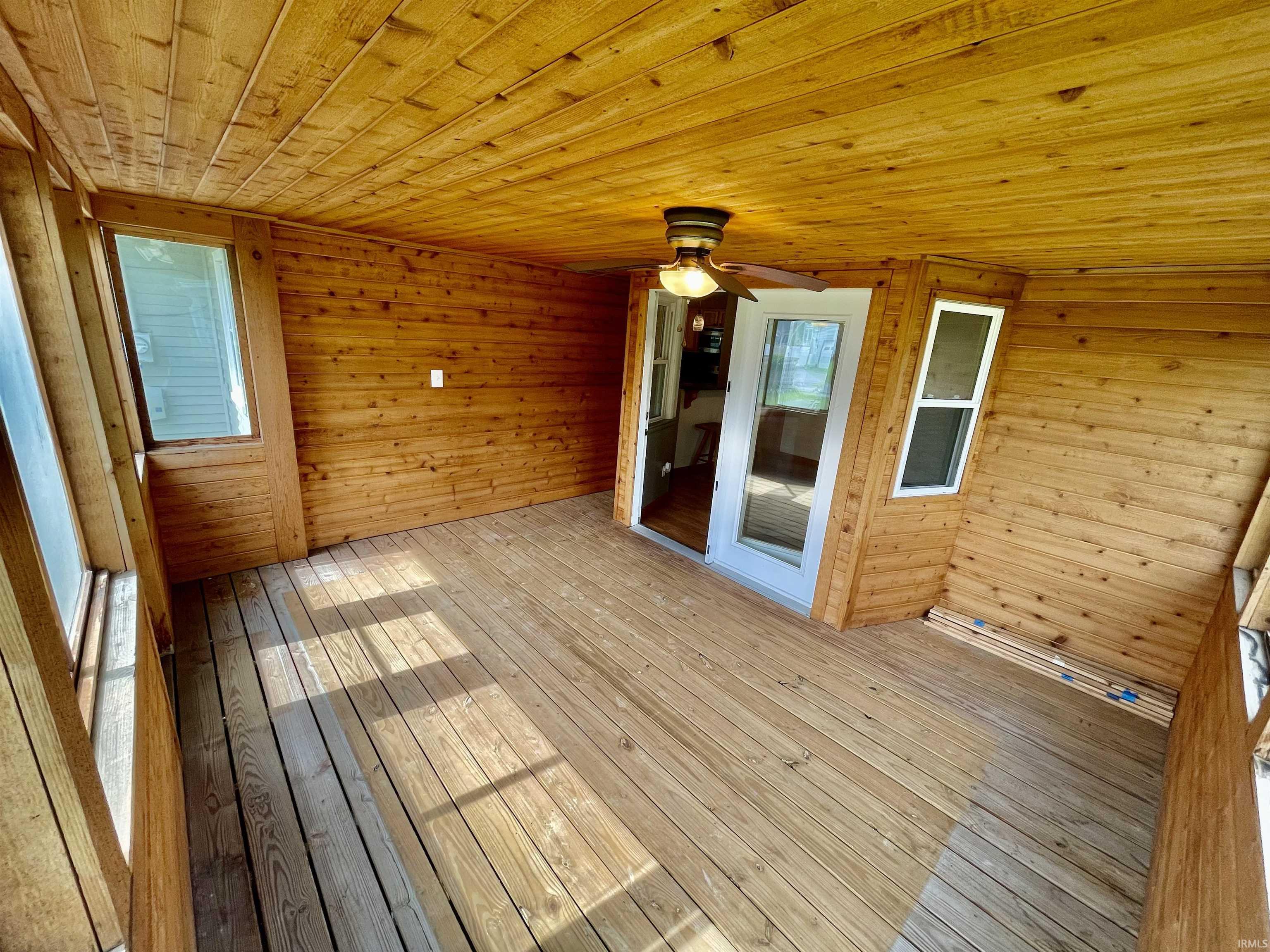 Wood-paneled screened porch featuring a ceiling fan, multiple windows, and a glass-paneled door