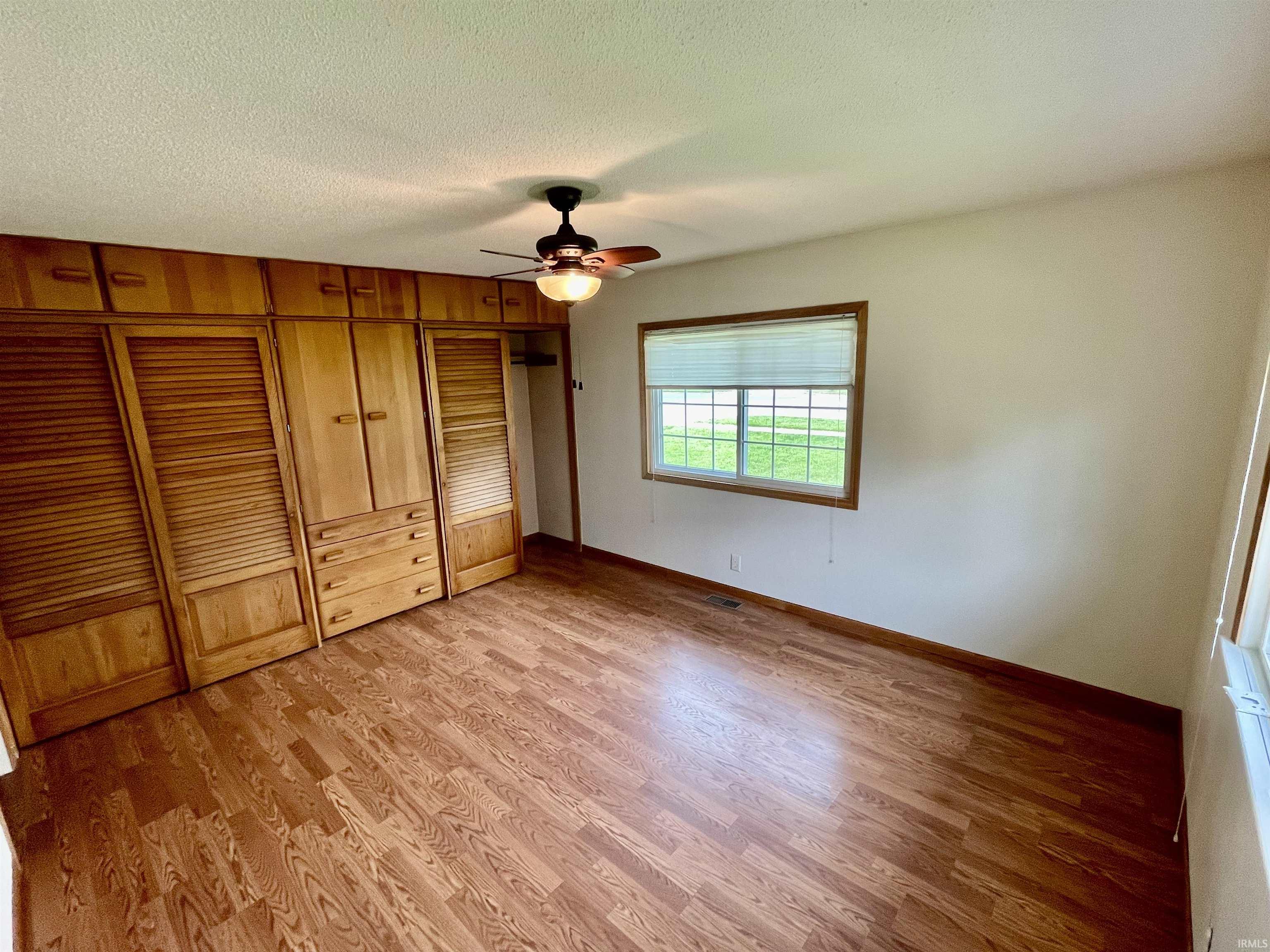 Bedroom featuring wood-finish flooring, a ceiling fan with integrated lighting, and a large window with blinds