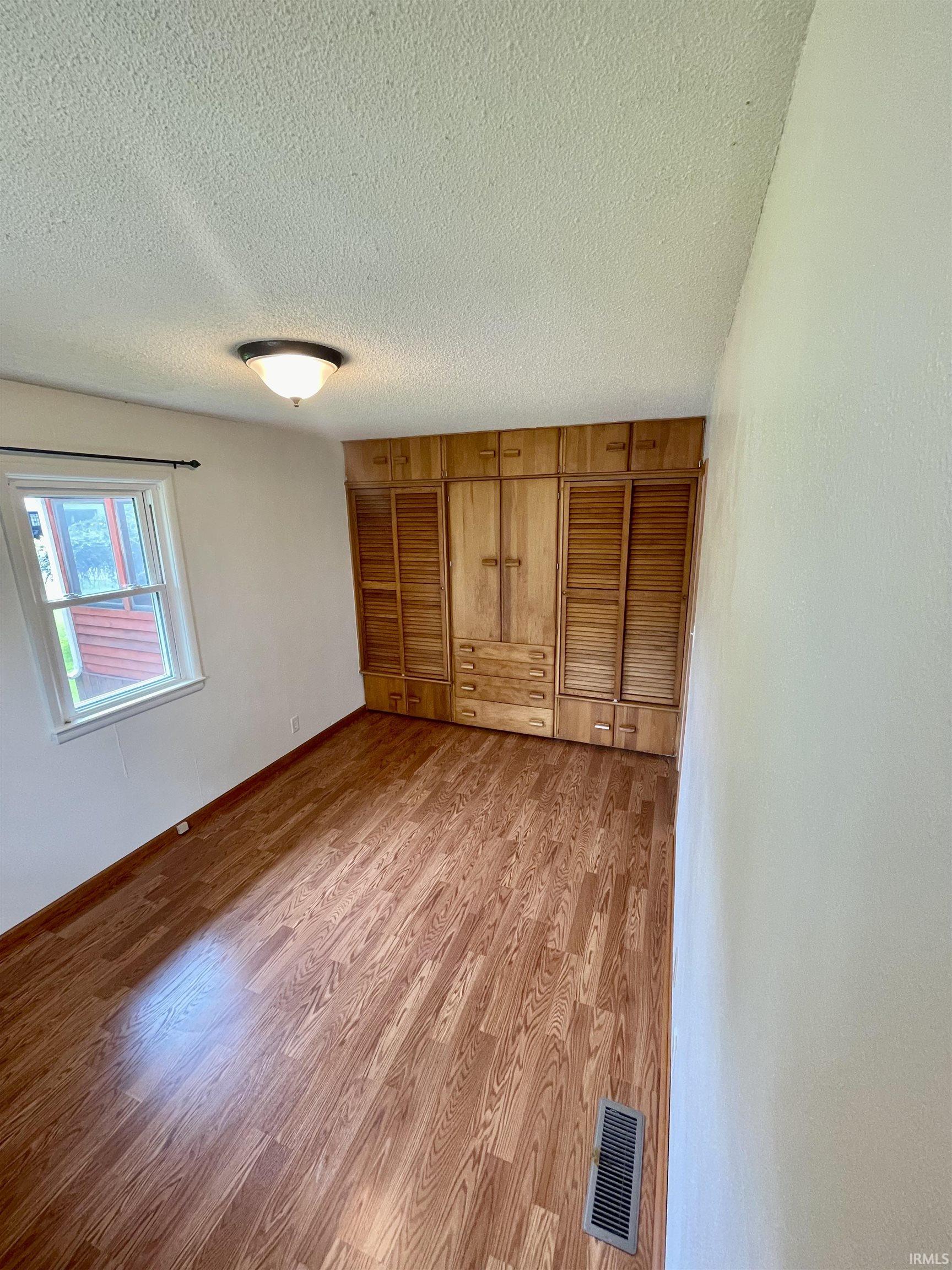 Light-filled room featuring wood-finish flooring and a full wall of built-in wood cabinetry with louvered doors