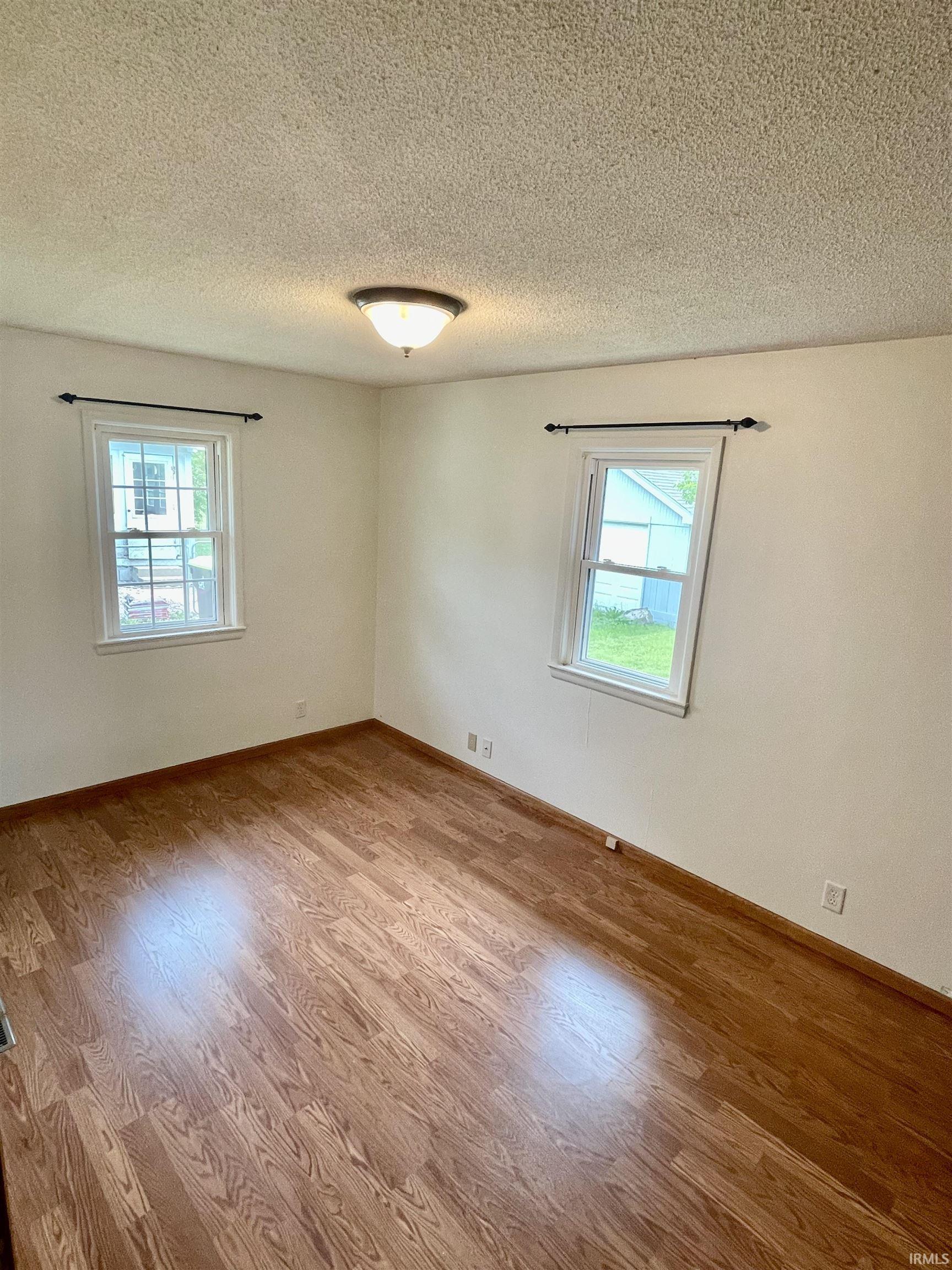 Room featuring wood-finish flooring, white walls, and two windows