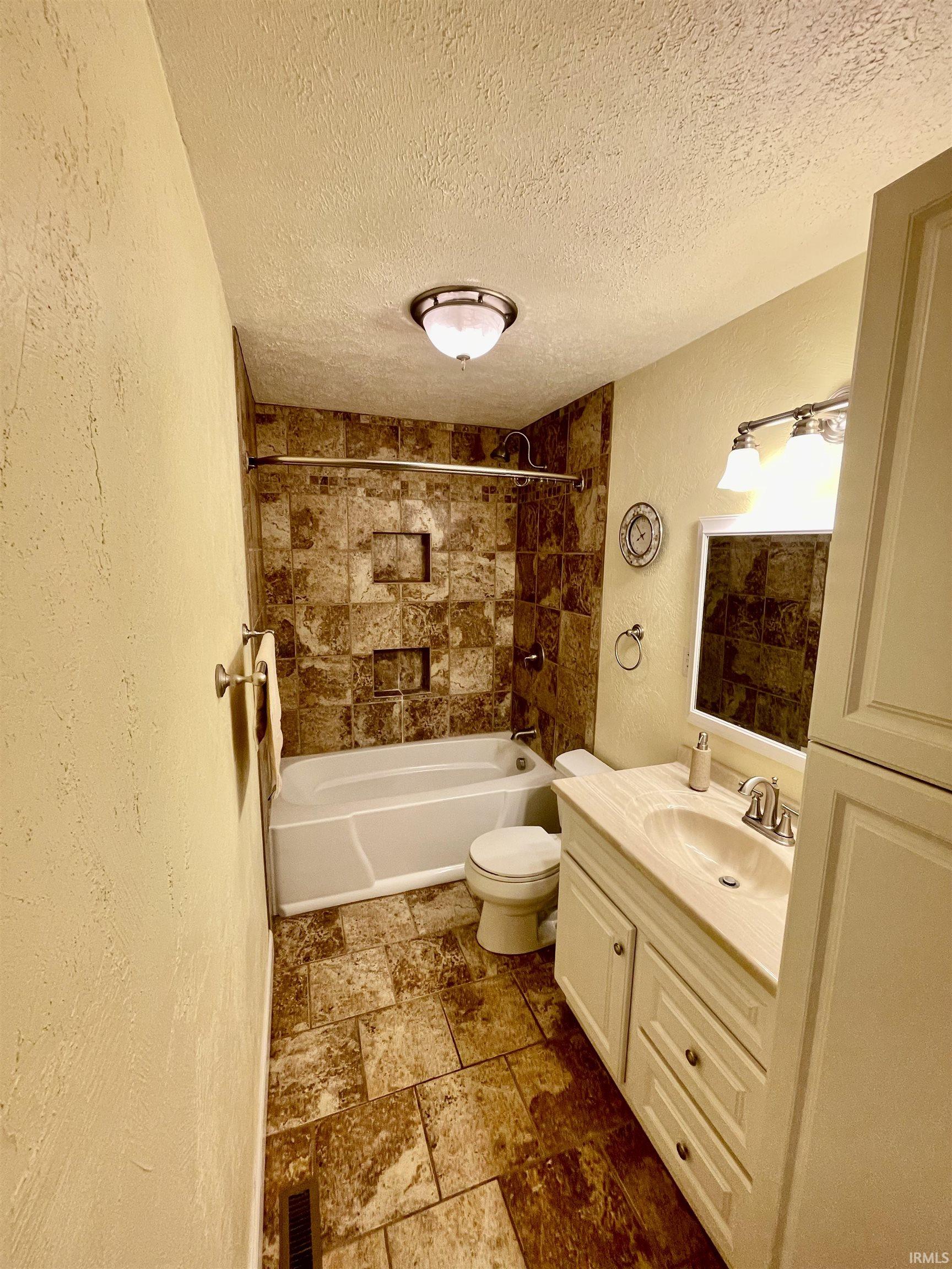 Bathroom featuring a white bathtub, a toilet, a vanity with a white countertop and integrated sink, and an overhead light fixture
