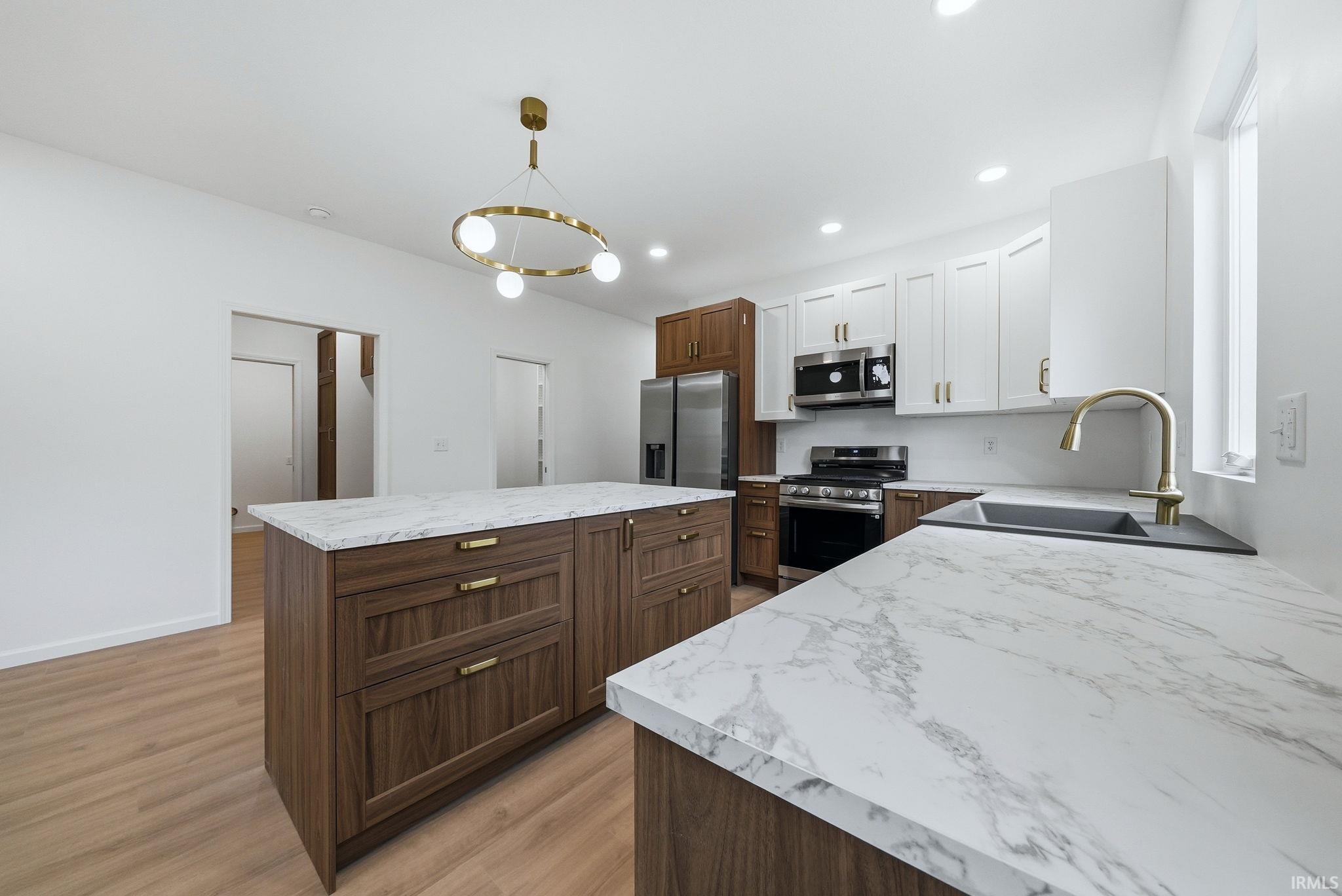 Kitchen featuring a central island with wood-finish cabinetry, faux marble laminate countertops, and a modern gold-tone chandelier
