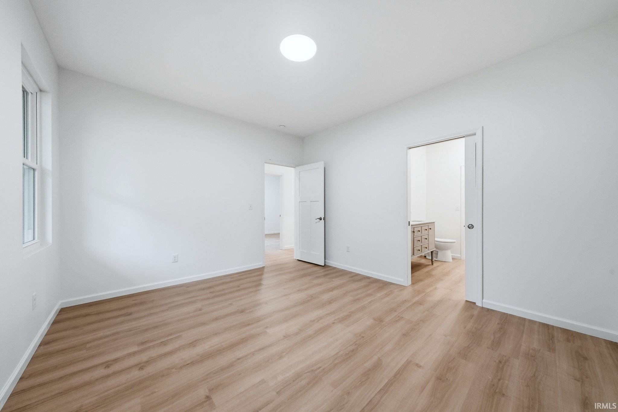 Spacious bedroom #1 featuring wood-finish flooring, white walls, a white trim baseboard, and a circular flush-mount ceiling light