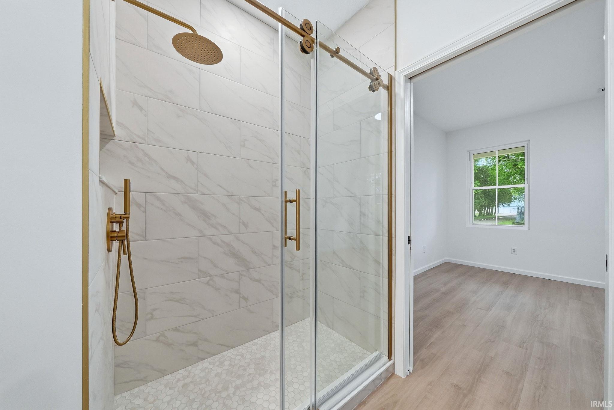 Ensuite features a walk-in shower with gold-tone hardware, large format tile walls, hex tile flooring, recessed niche, and a glass sliding door