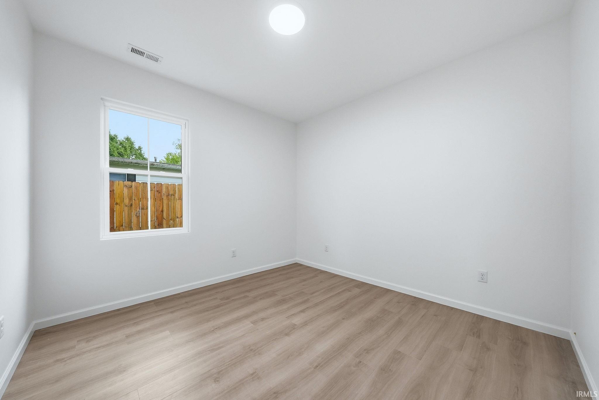 Bright bed/flex room featuring wood-finish flooring, white walls, and a single window