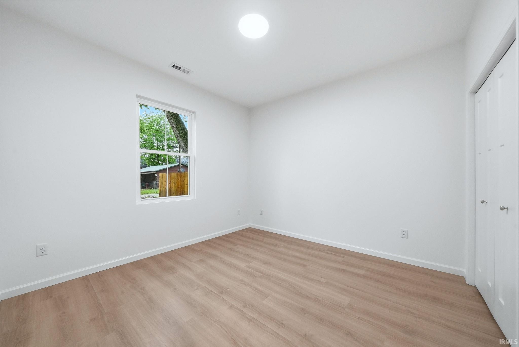 Bedroom featuring light wood-finish flooring, white walls, and a window offering exterior views