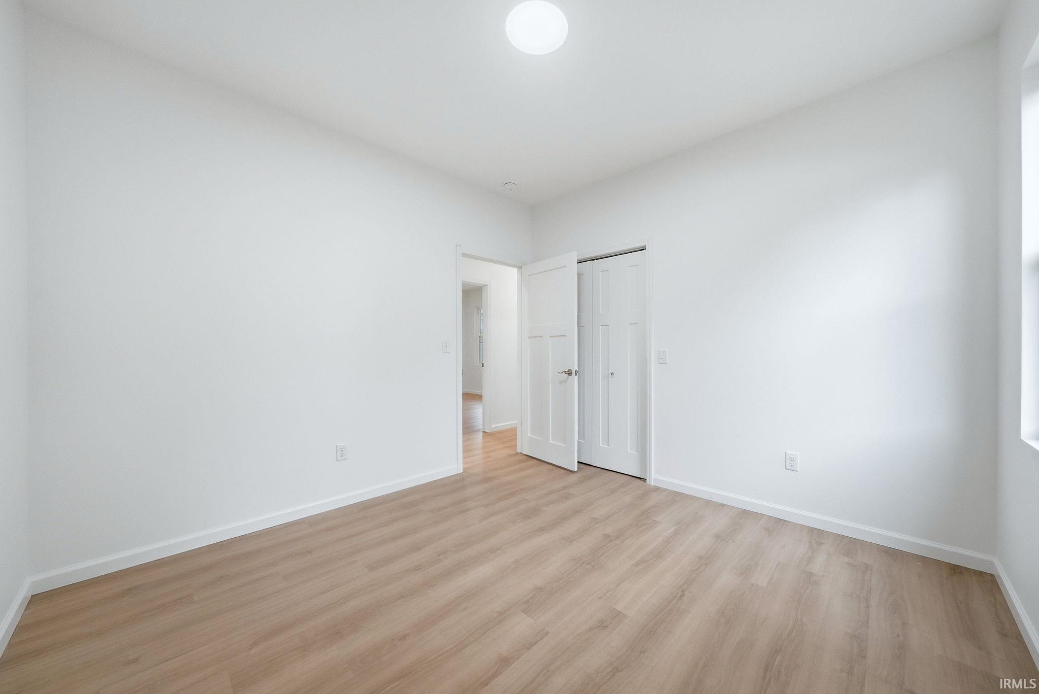 Bright bed/flex room featuring light wood-finish flooring, white baseboards, and a flush-mount ceiling light