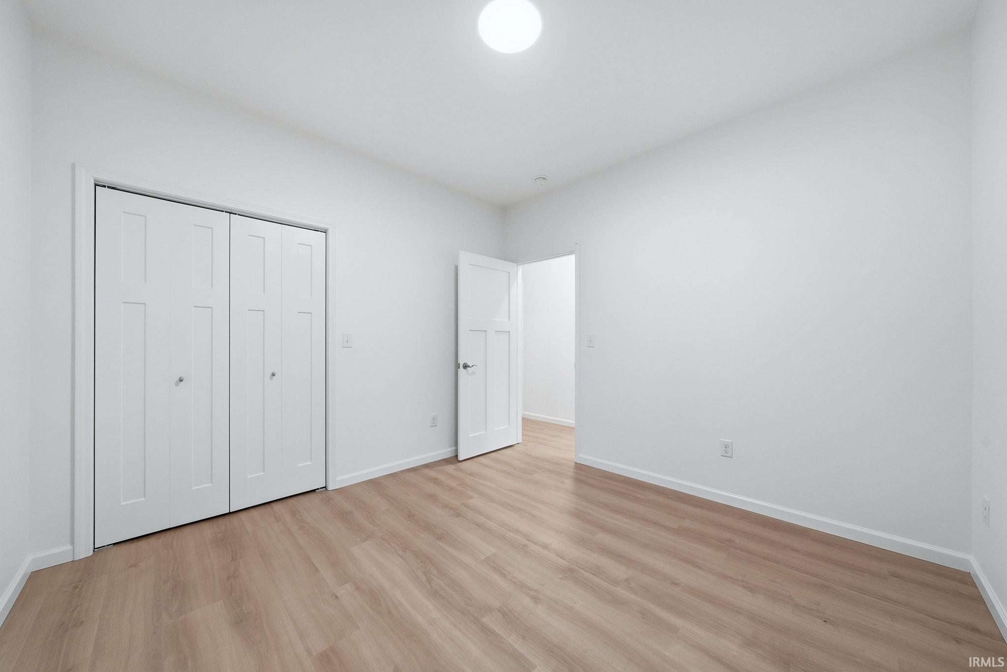 Bedroom featuring light wood-finish flooring, white walls, and a contemporary ceiling light fixture