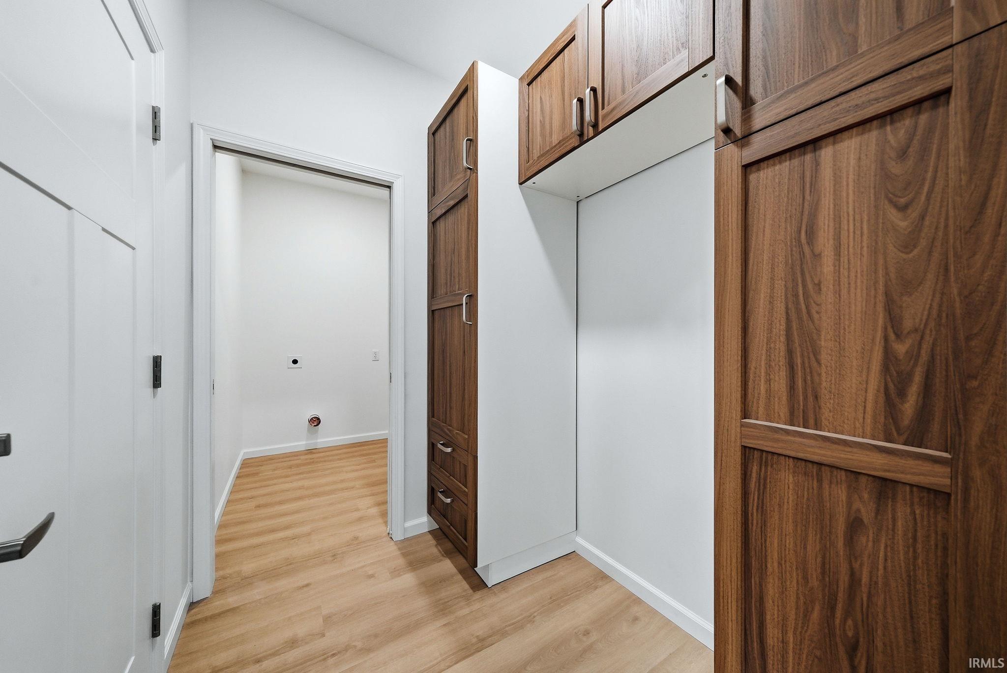 Hallway leading from laundry featuring wood-finish flooring, white walls, and built-in cabinetry with wood-grain doors and metal hardware