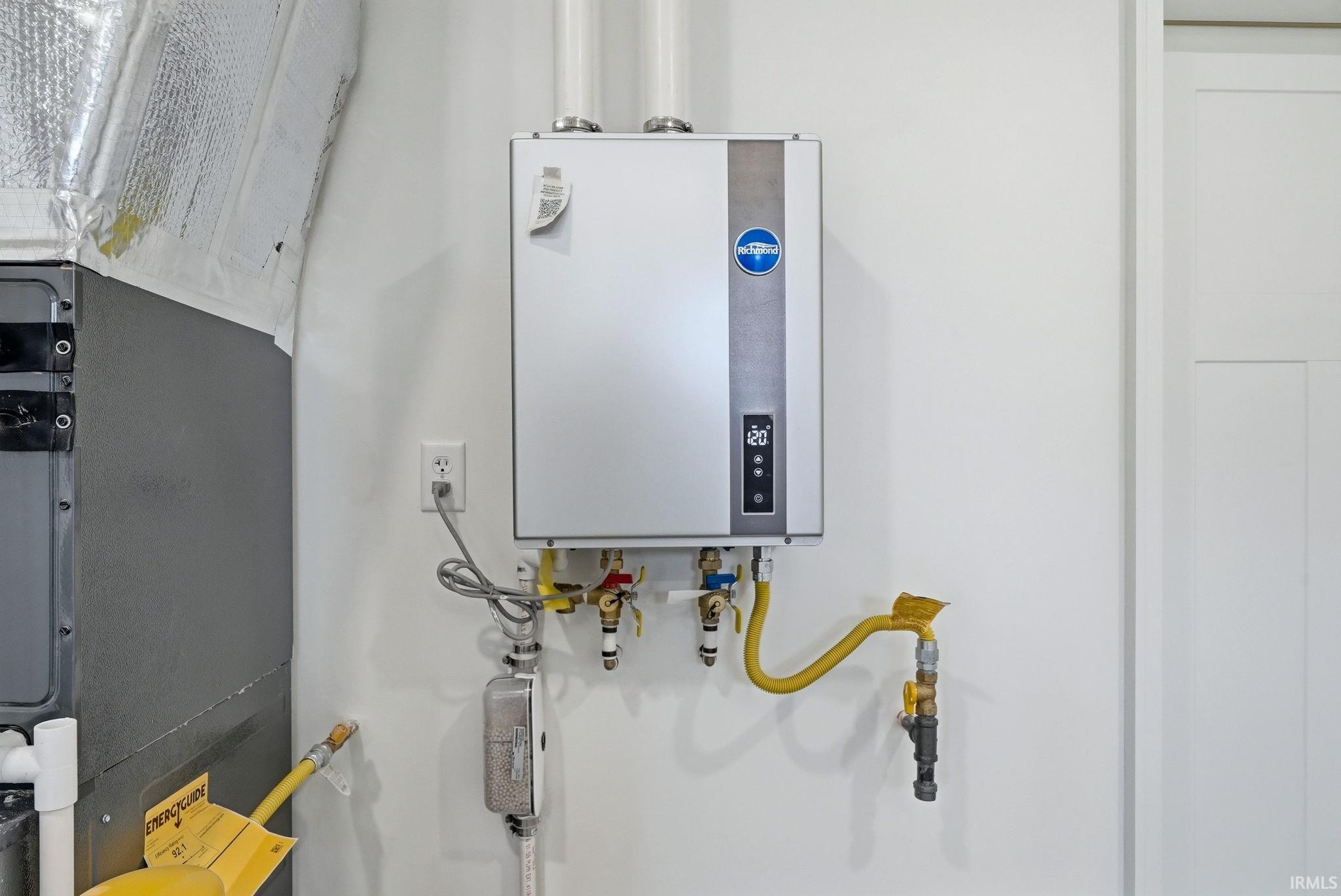 Wall-mounted tankless water heater with digital display housed in garage along with furnace and side door access