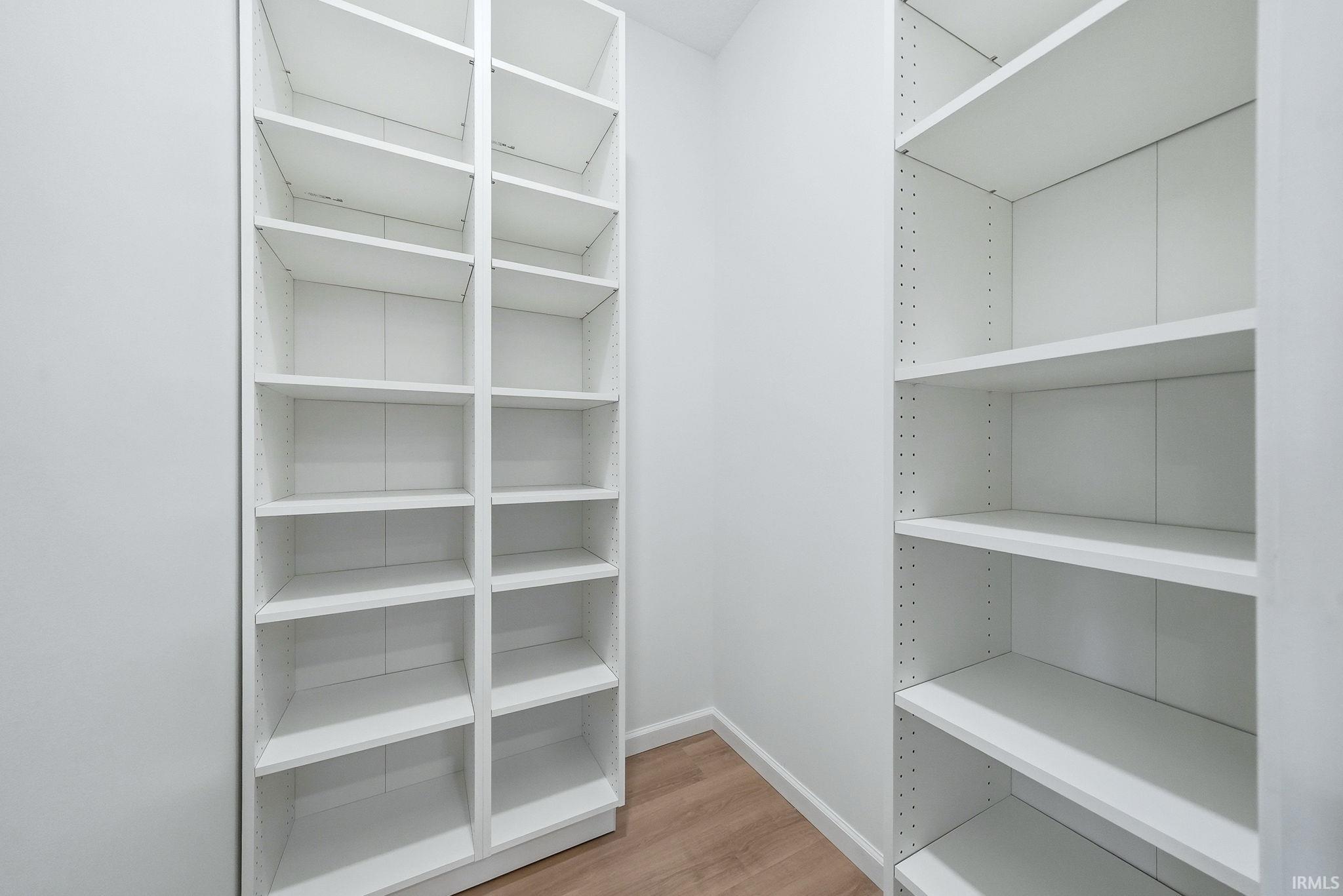 Walk-in closet featuring white built-in shelving, light wood-finish flooring, and white baseboards