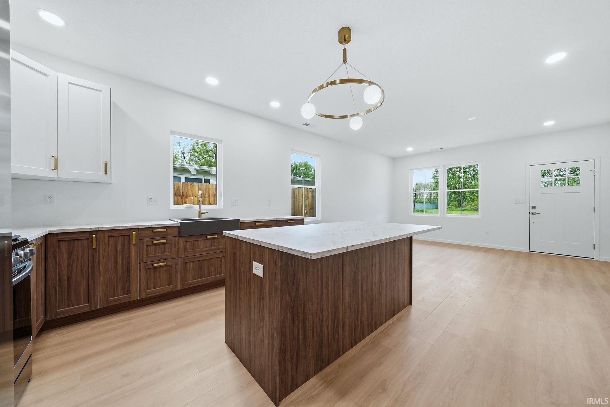 Open-concept kitchen and living area featuring a large center island with two-tone cabinetry, stainless steel appliances, and light wood-finish flooring