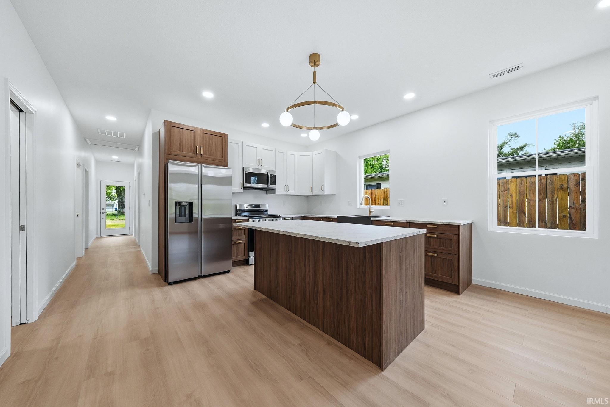 Modern kitchen featuring a central island with stainless steel appliances, two-tone cabinetry, and wood-finish flooring