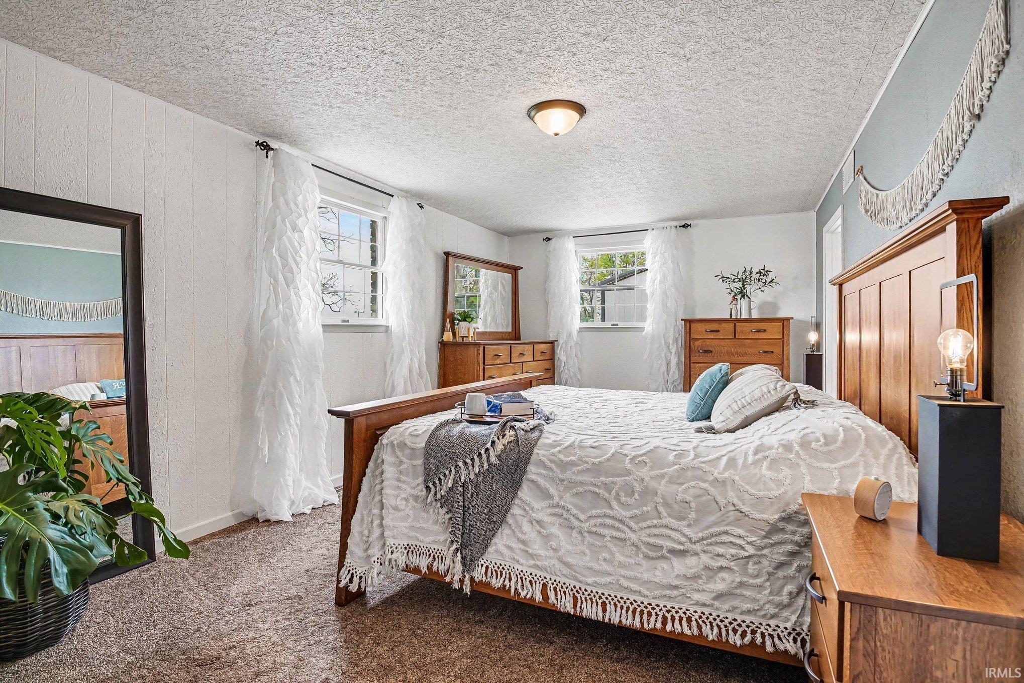 Bedroom featuring two window openings with white trim, textured wall paneling, and a flush-mount ceiling light fixture