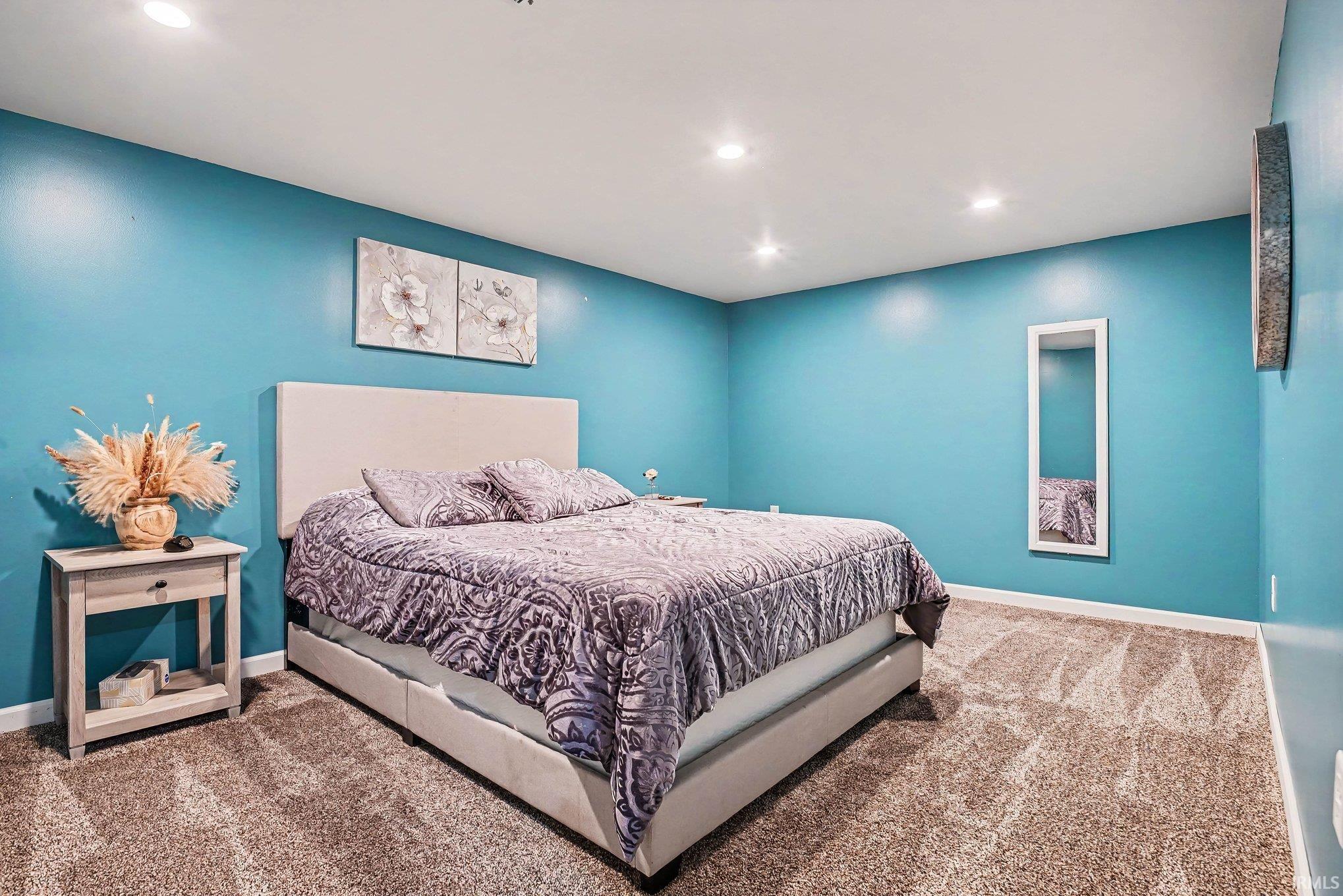 Recessed lighting illuminates a room featuring teal walls and plush carpet flooring