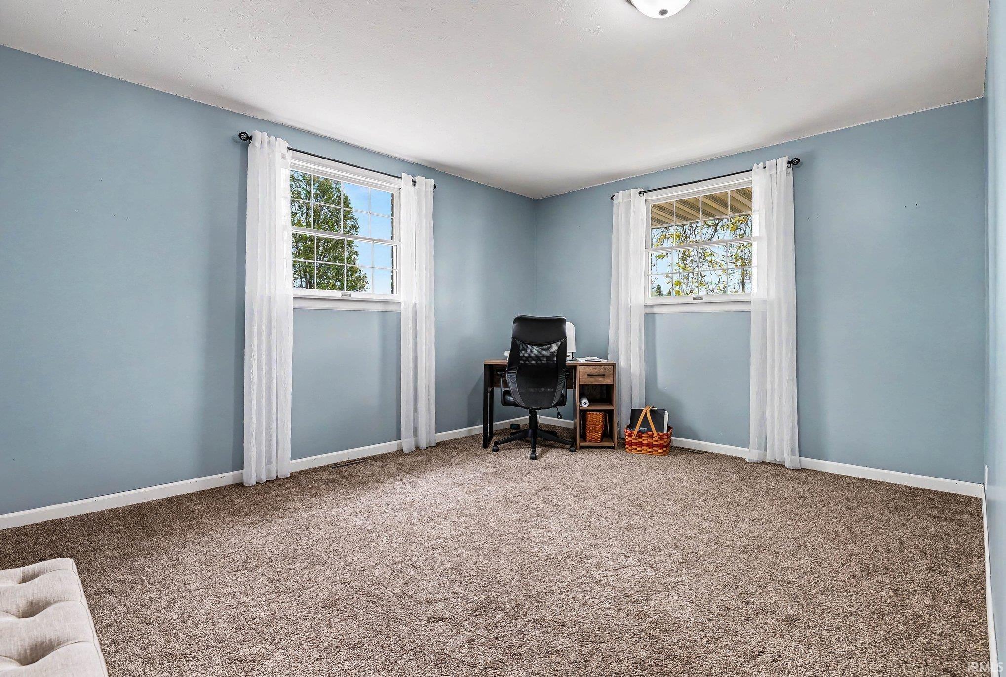 Room featuring two large windows with white trim, light blue painted walls, and textured carpeting