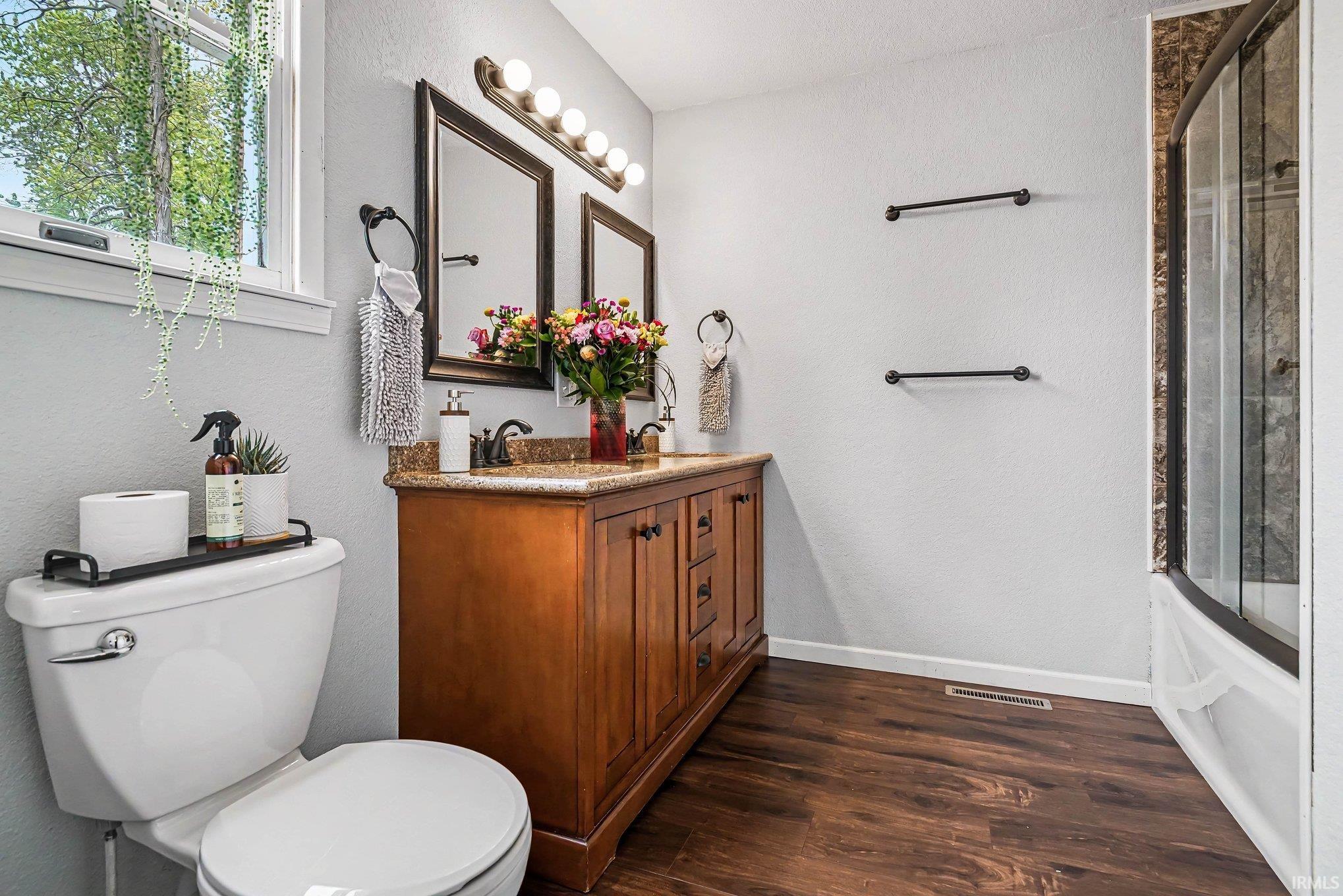 Bathroom featuring a double vanity with wood cabinetry and a stone-finish countertop, dual mirrors, and a multi-bulb light fixture