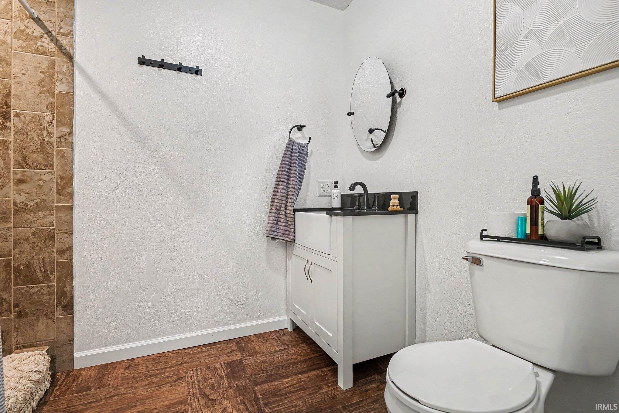 Bathroom featuring a white vanity with a dark countertop and black faucet, a toilet, and wood-finish flooring