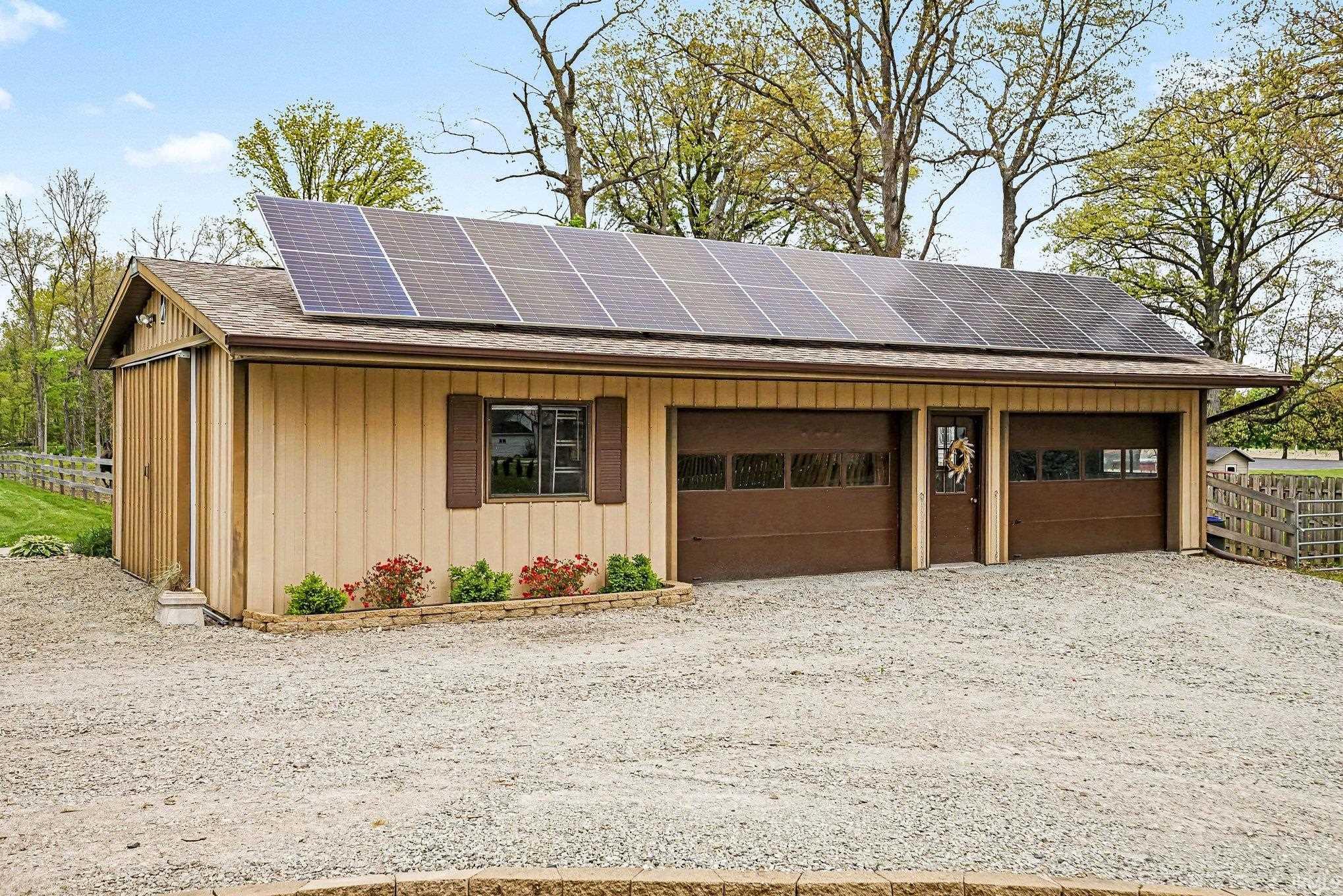 Detached outbuilding with extensive solar panel array, two garage bays, board and batten siding, and a gravel driveway