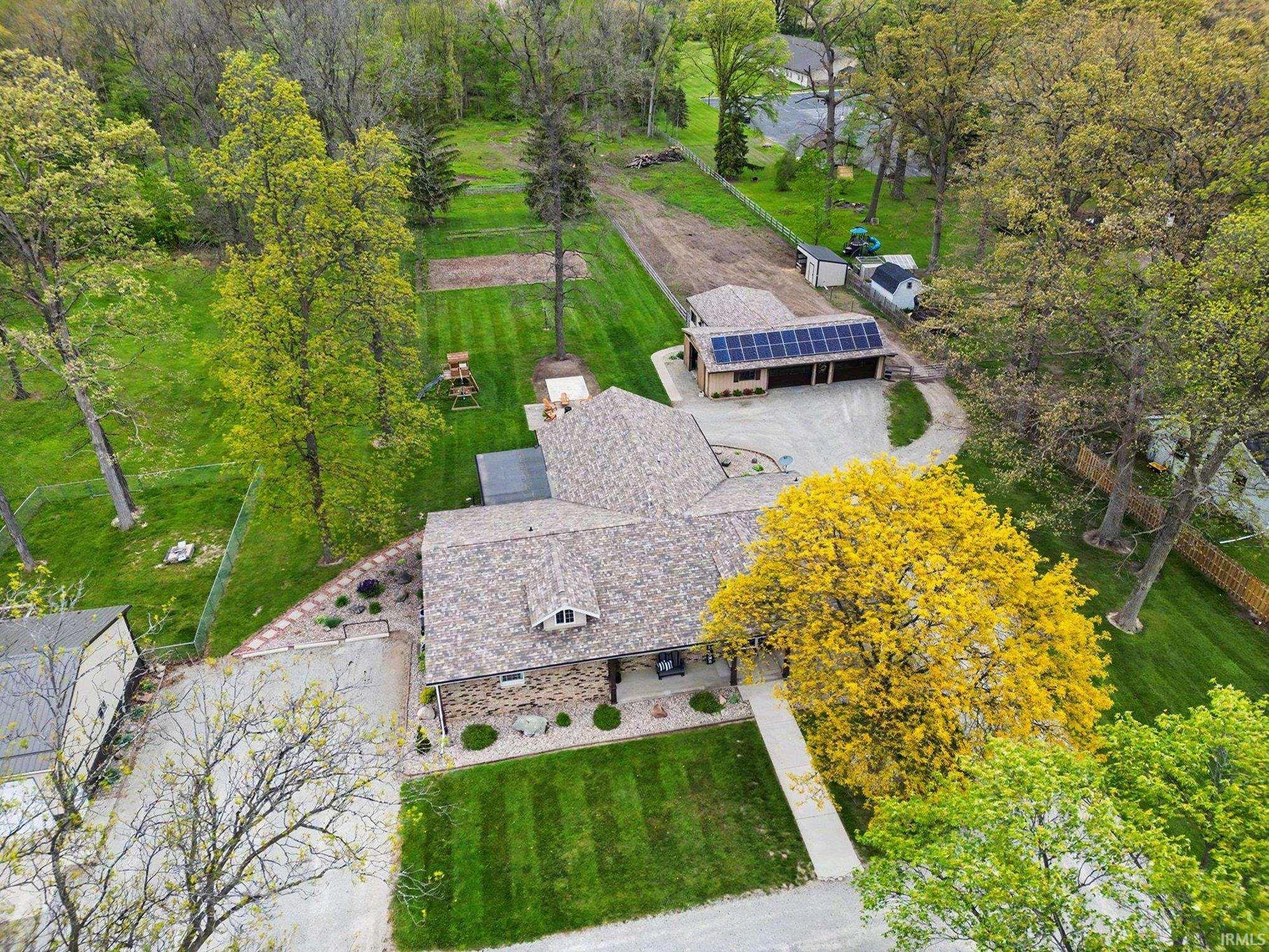 Expansive property featuring a stone and siding exterior, a multi-car detached garage with solar panels, and extensive manicured lawns