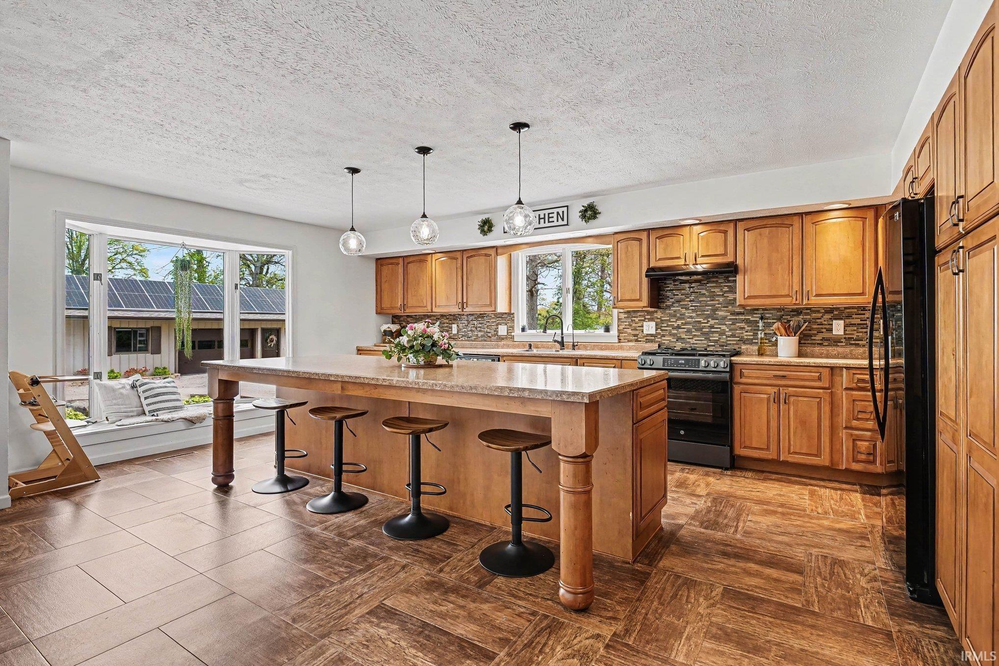 Kitchen featuring a central island with seating, a built-in window bench, light wood-finish cabinetry, black appliances, and patterned tile flooring