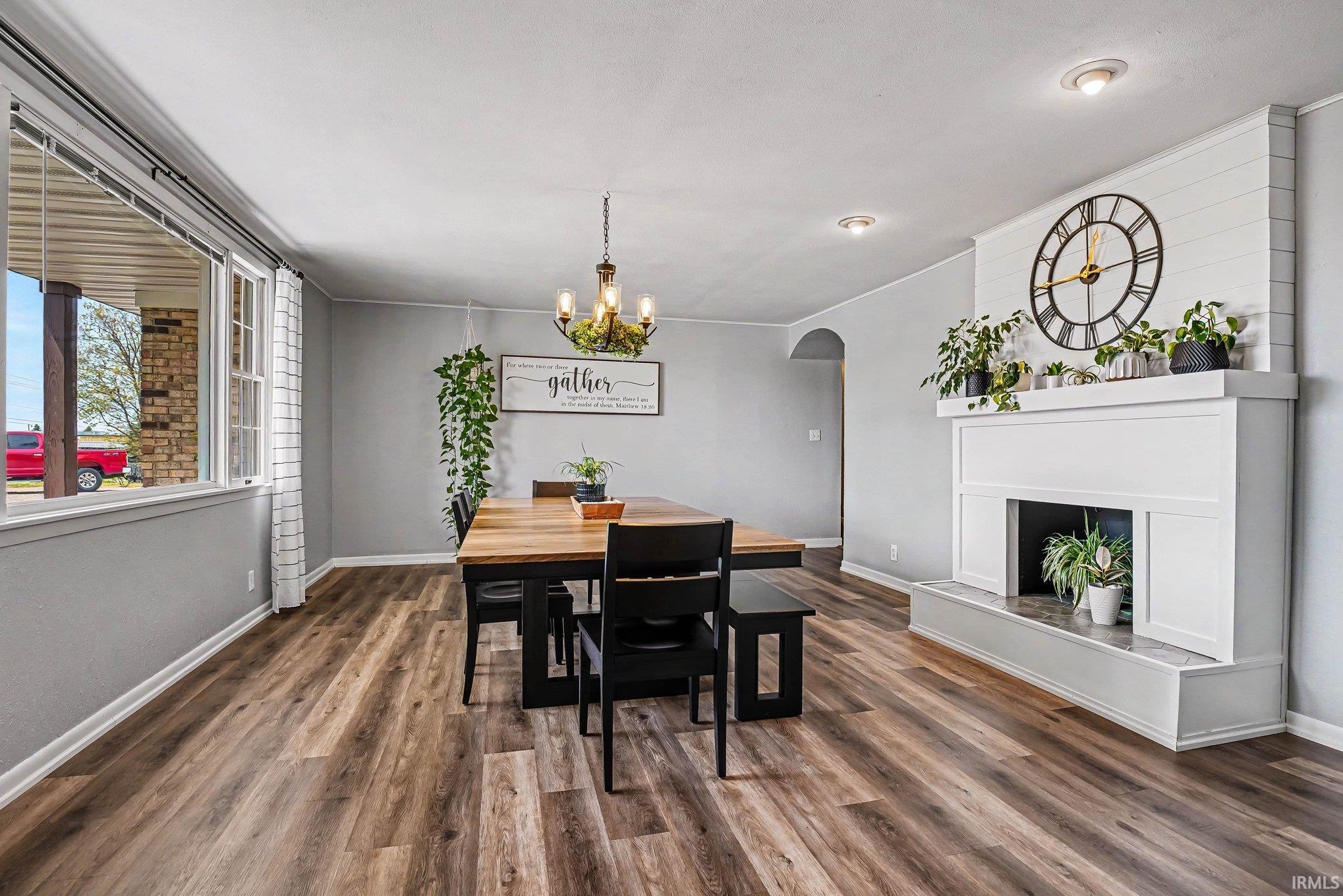 Spacious room featuring wood-finish flooring, a prominent white fireplace with a shiplap accent wall, and a large window offering natural light