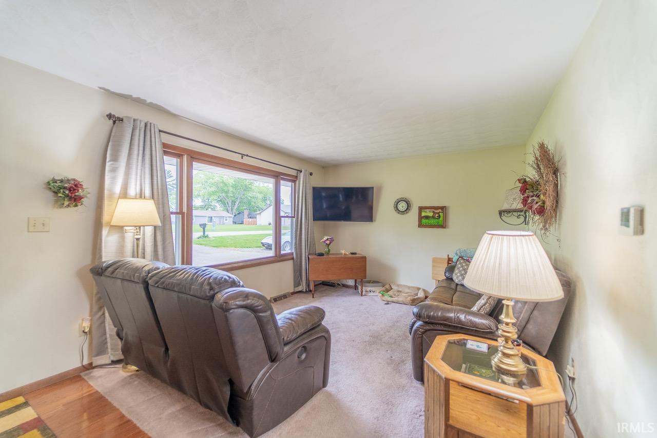 Spacious living area featuring a large picture window, light-toned walls, and mixed flooring with wood-finish sections
