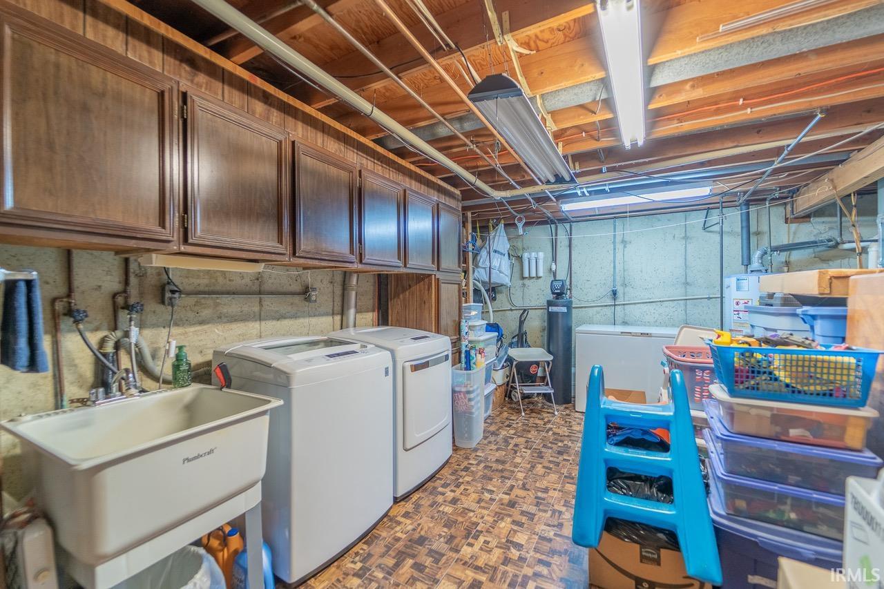 Utility room featuring a laundry sink, overhead cabinetry, exposed ceiling joists, and concrete walls