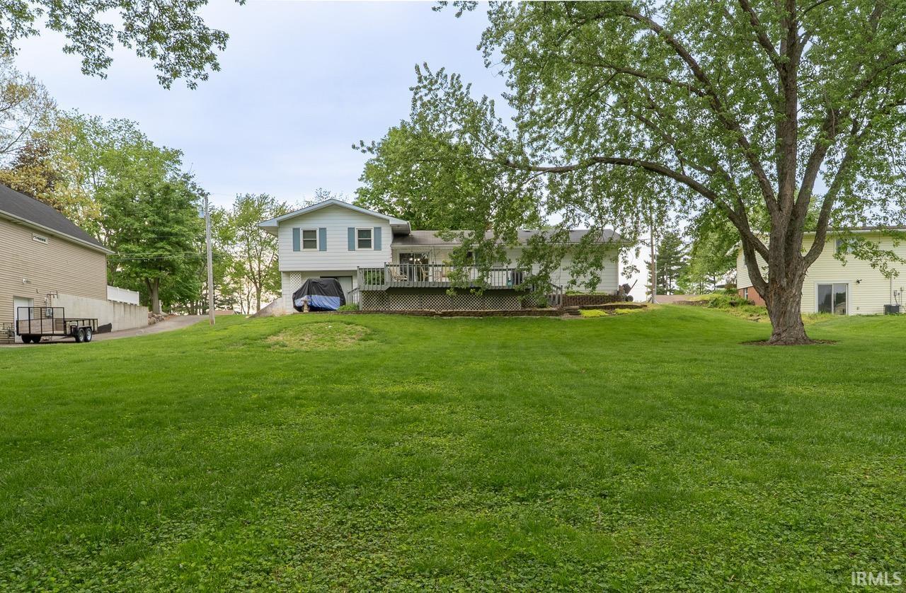 Expansive green lawn with mature trees and a two-story home featuring light blue shutters and a ground-level garage